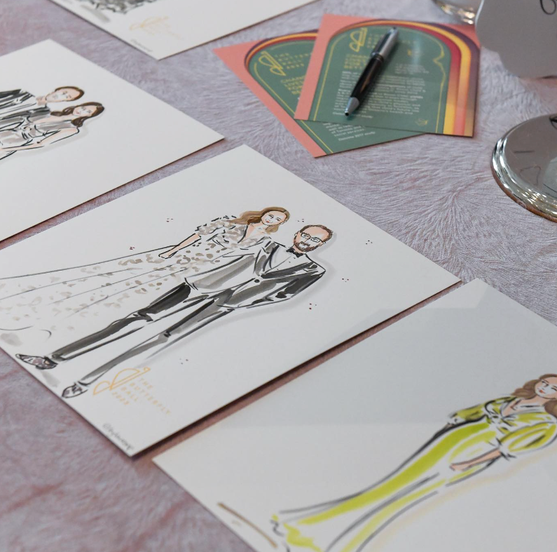 Wedding invitation cards featuring illustrated couple sketches laid out on a gray surface.