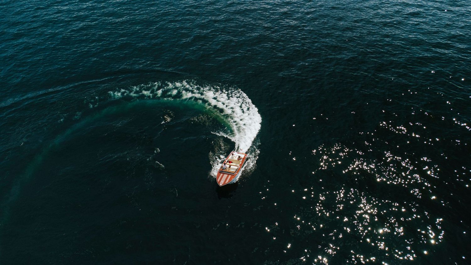 A surfer rides a towering wave breaking in deep blue ocean waters with white spray trailing behind.