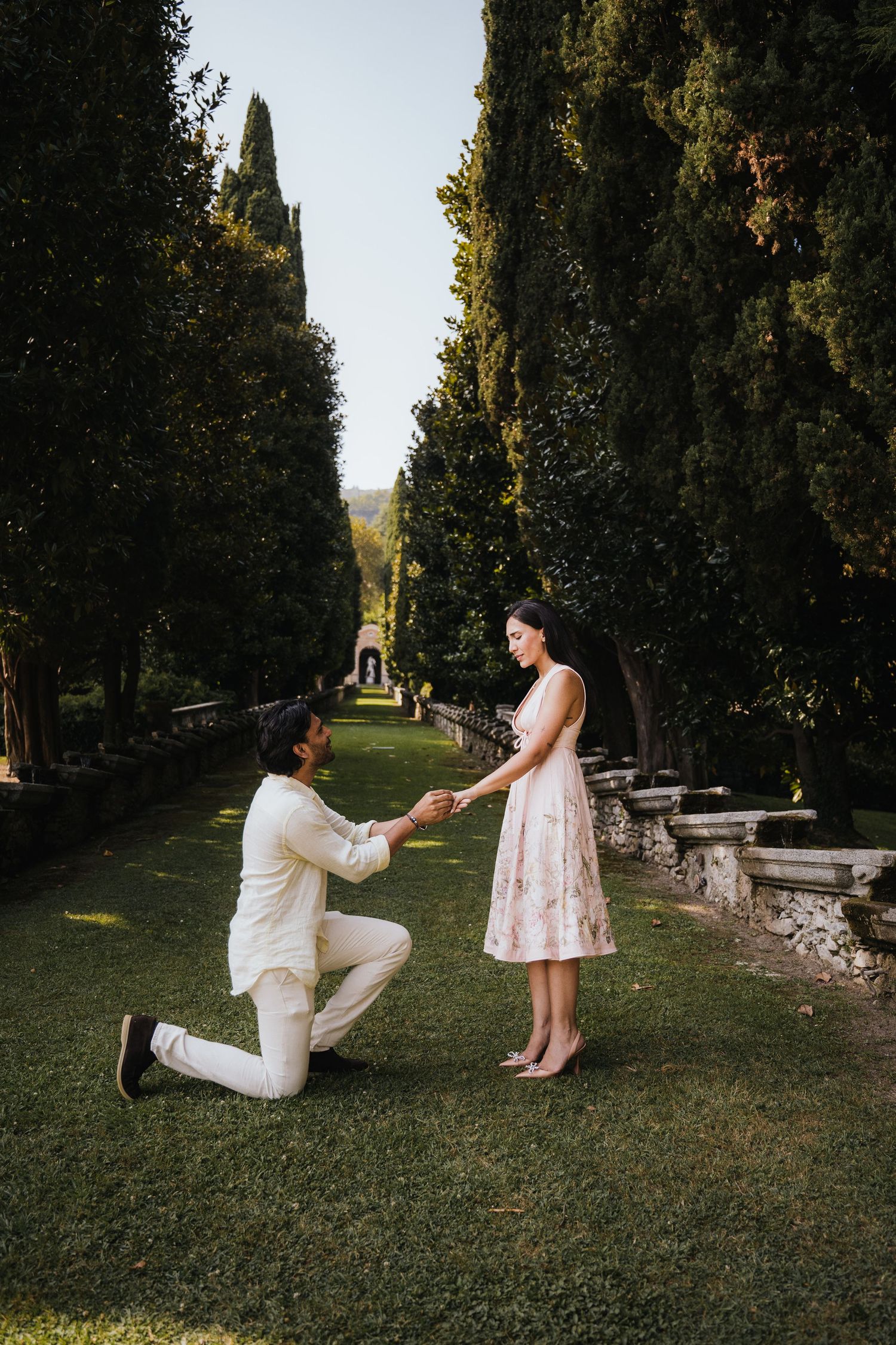 Marriage proposal sequence in garden pathway lined with cypress trees.