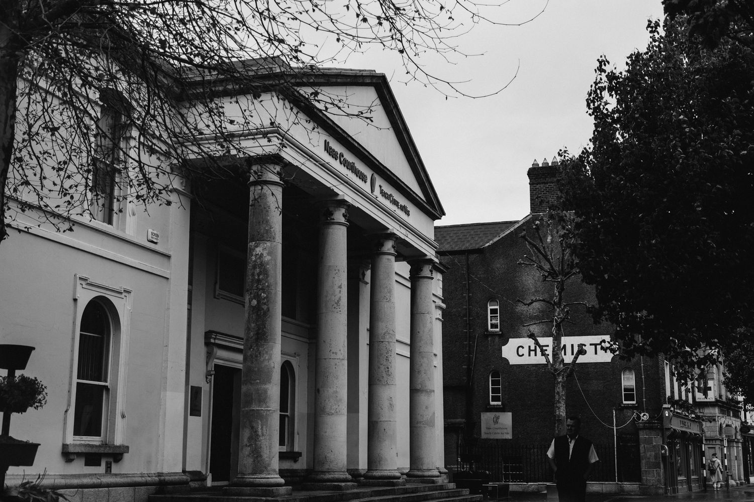 Black and white photo of a historic building with classical columns and triangular pediment in an urban setting.