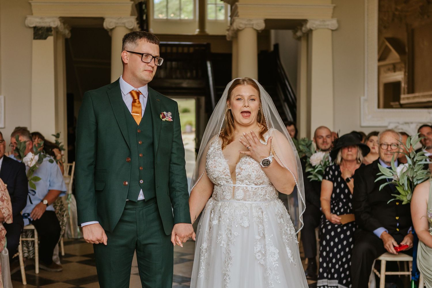 A joyful moment during a wedding ceremony shows a couple reacting with excitement in a traditional venue setting.