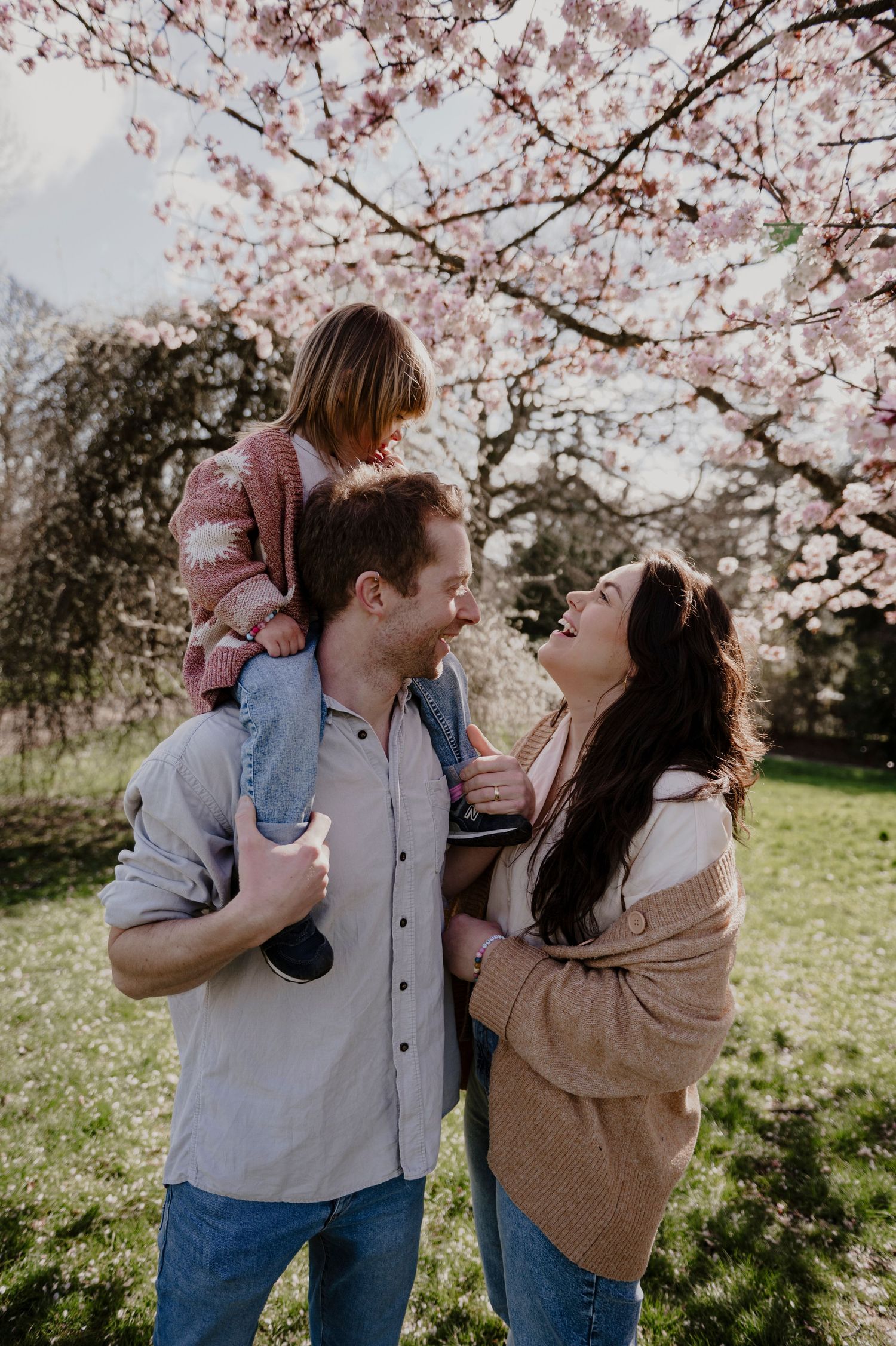 A family shares a playful moment under blooming cherry blossoms in springtime.