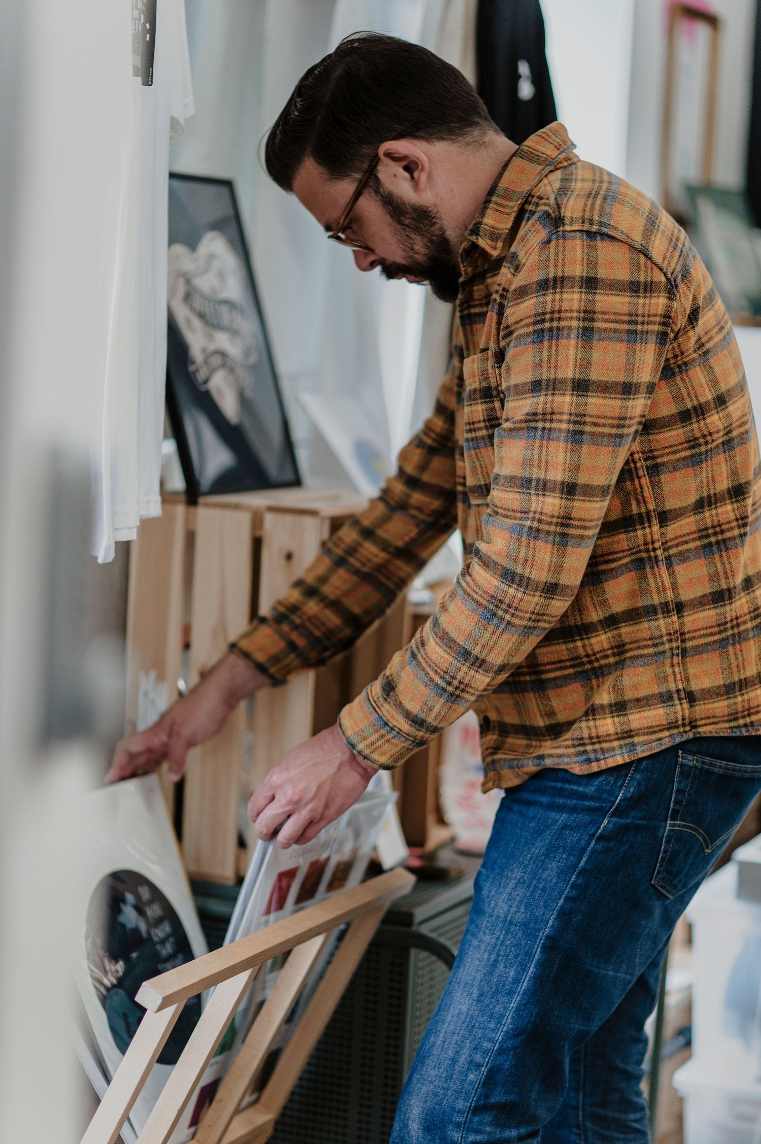 Person in plaid shirt browsing through vinyl records or artwork in a home setting.