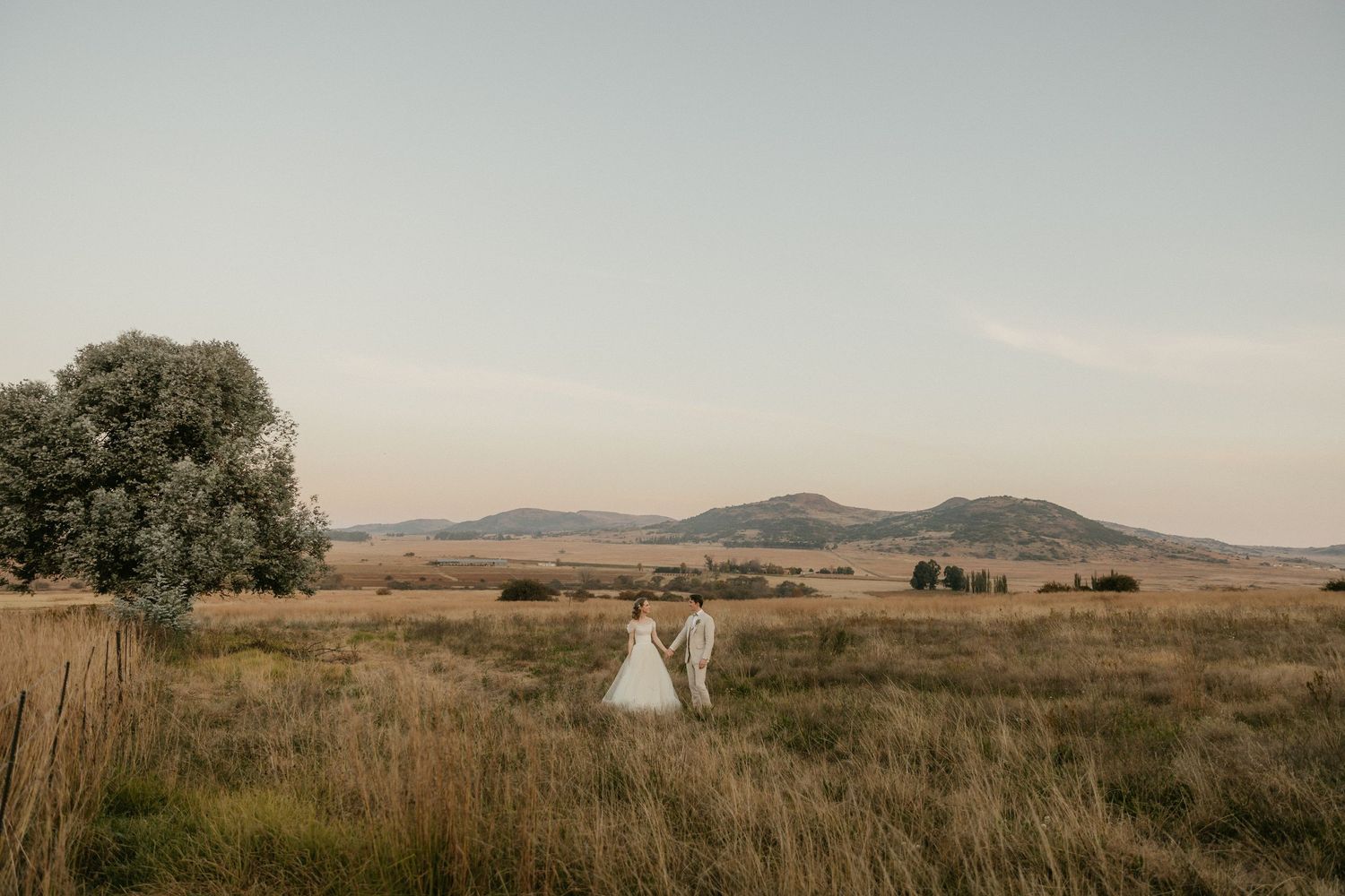 A picturesque countryside wedding portrait with rolling hills and golden grass in the background during sunset.