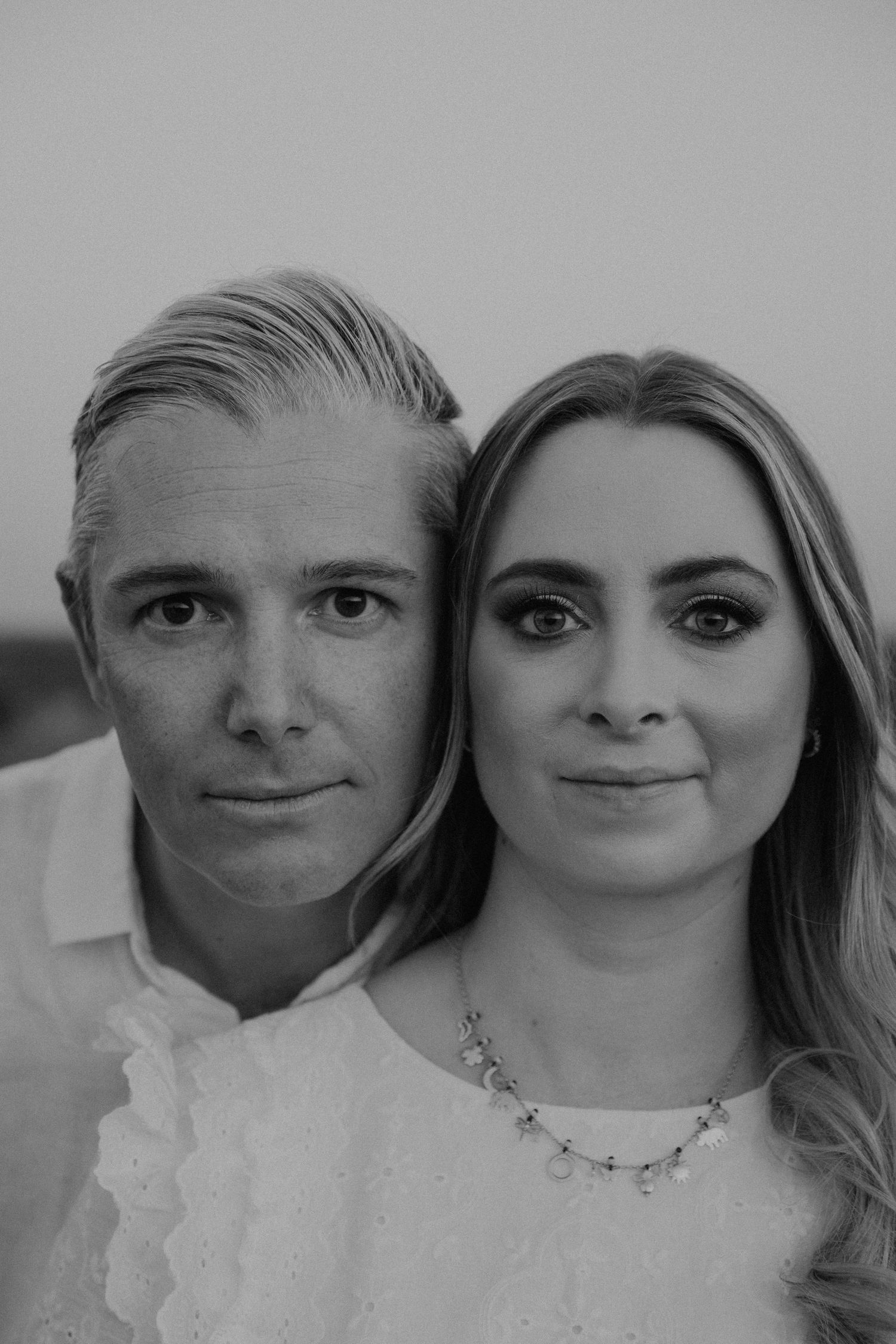 A black and white portrait of a couple in formal attire with the woman wearing a delicate necklace.