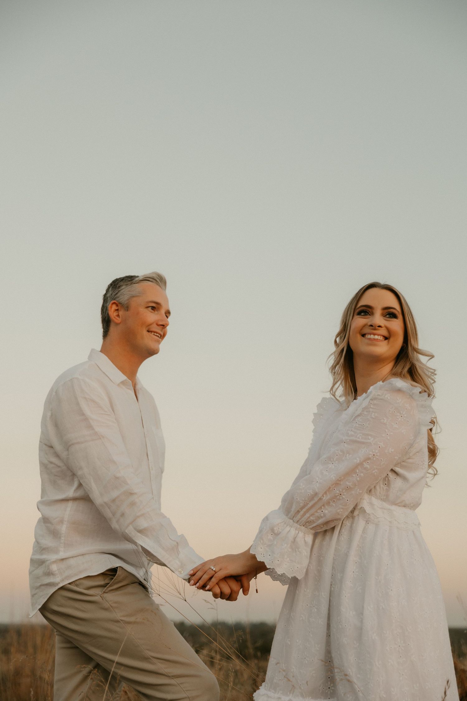 Couple in white outfits sharing a tender moment during sunset on an outdoor field.