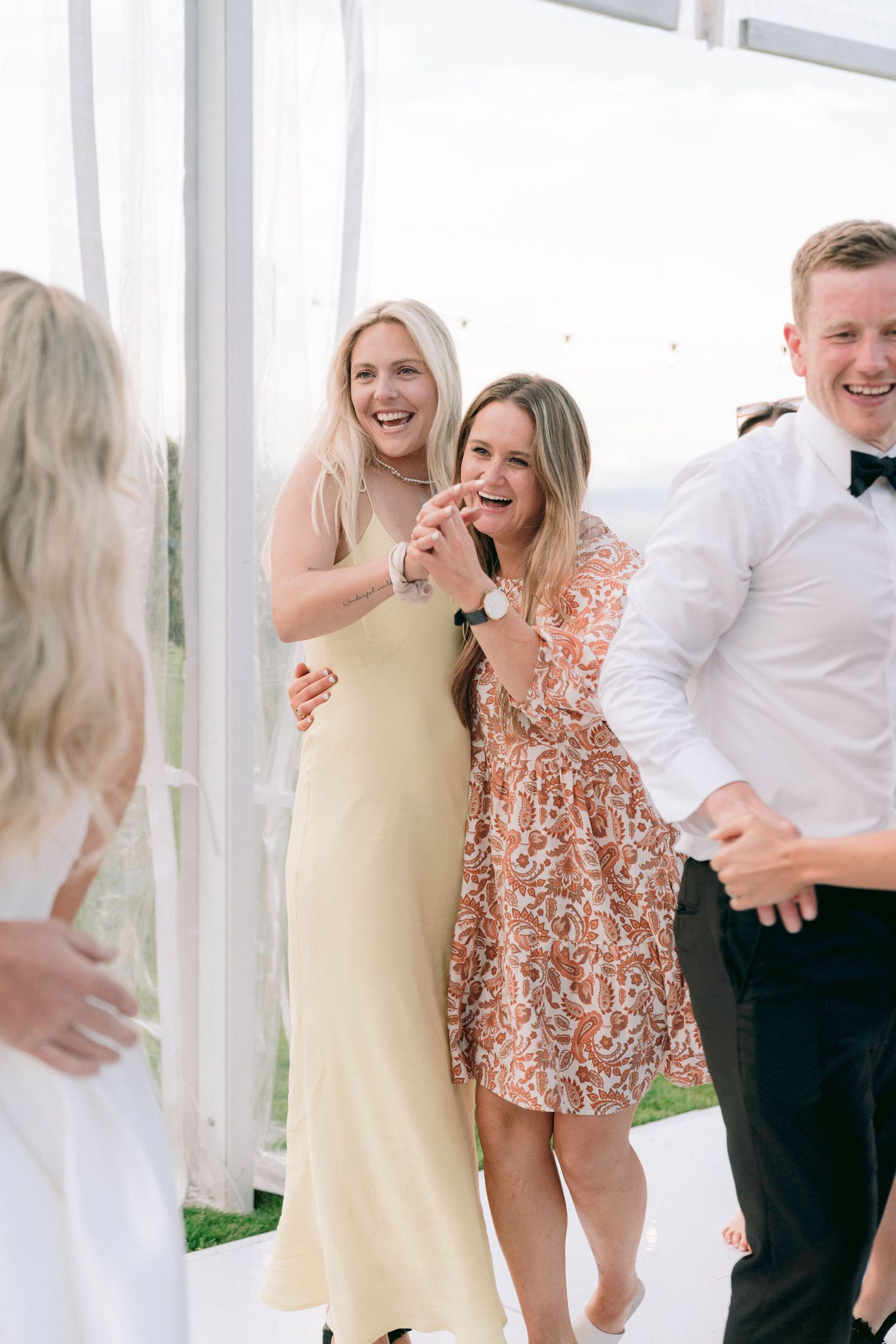 Wedding guests sharing laughter and dancing during a reception celebration in a white tent venue.