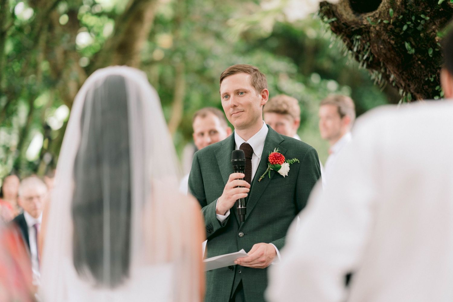 An outdoor wedding ceremony with guests gathered under trees.
