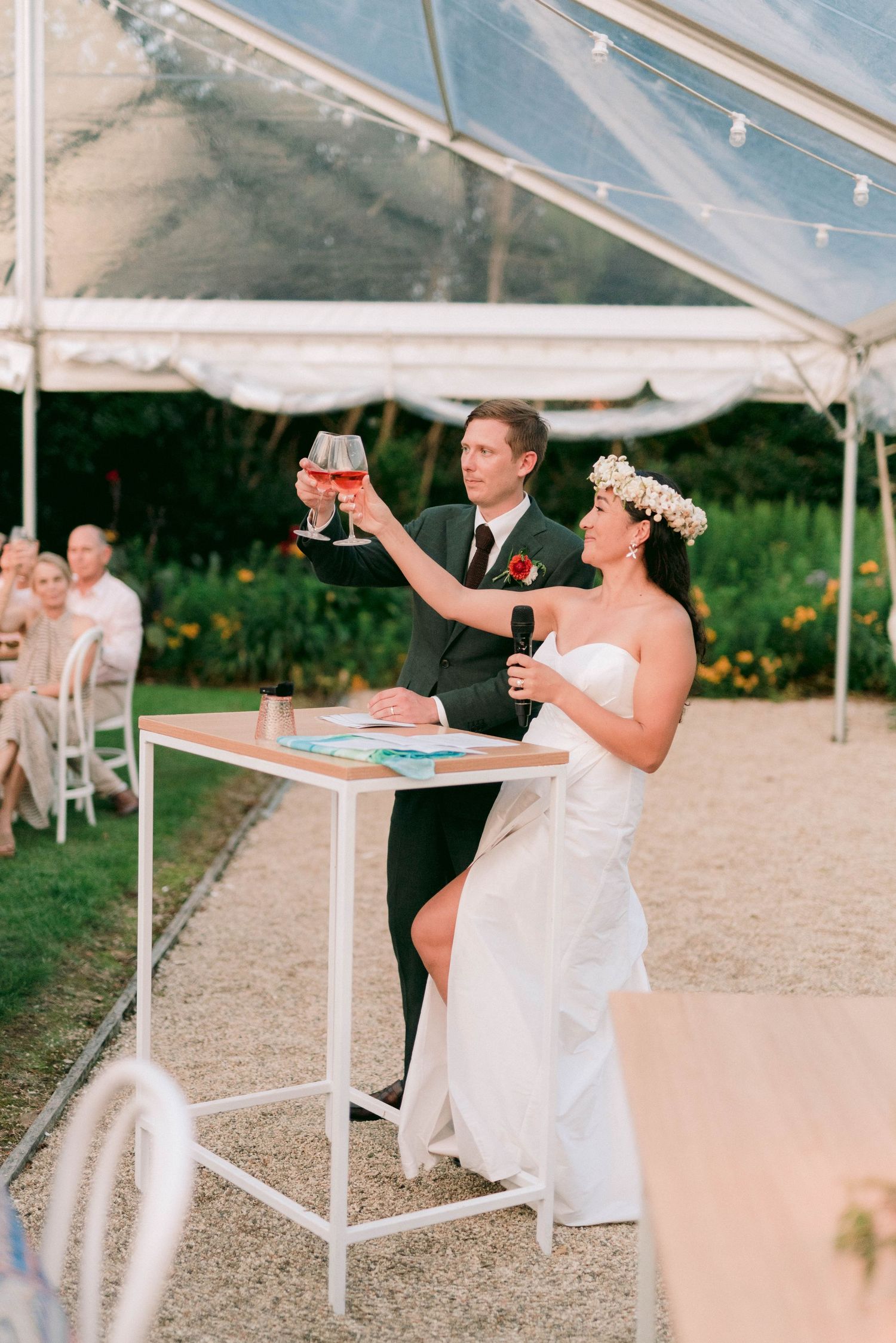 Couple making a toast at their wedding reception under a clear-top tent.