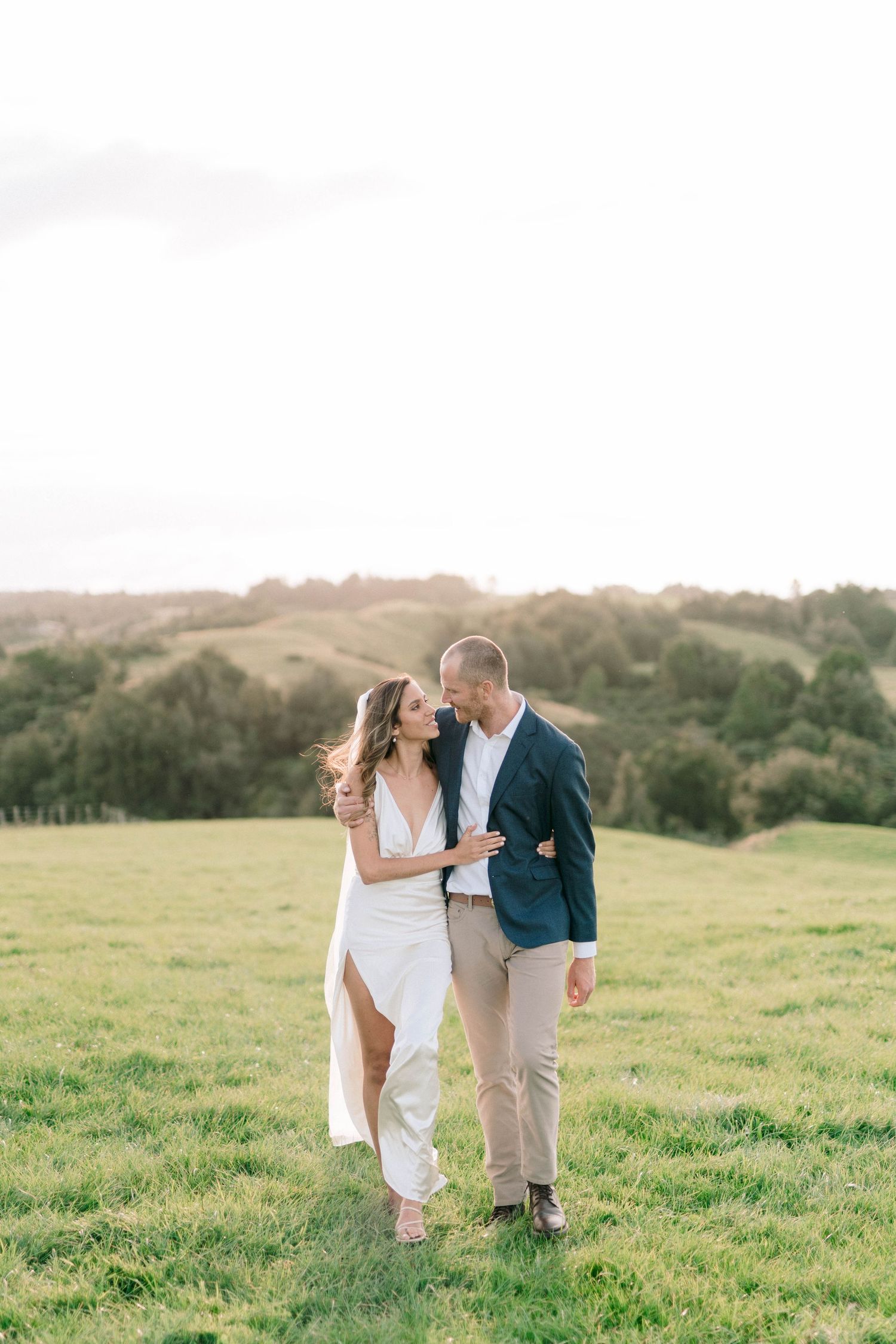 Newlyweds share intimate moments in a scenic hilltop meadow at sunset.