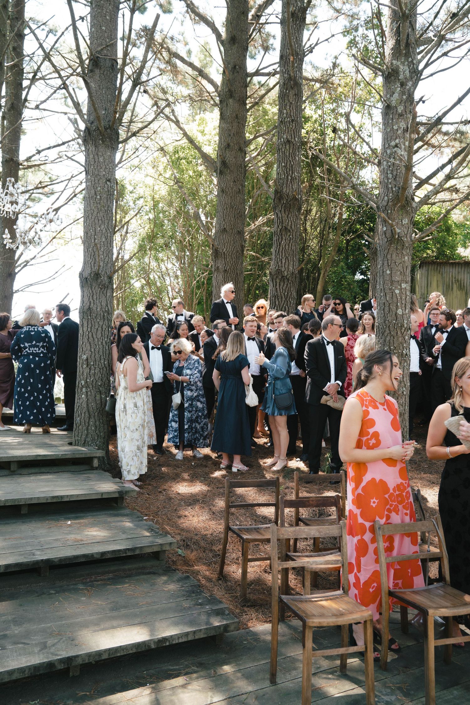 Outdoor wedding ceremony with guests gathered on wooden platforms among tall trees.