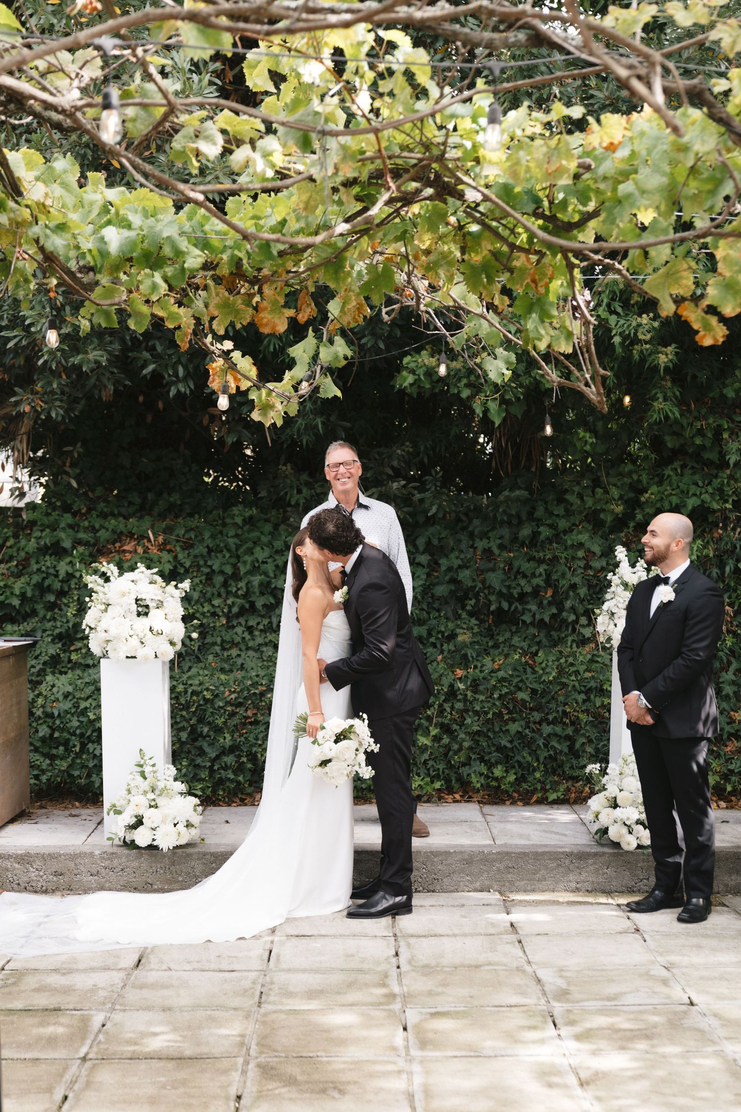 Couple exchanging vows under floral-decorated arch during outdoor wedding ceremony.