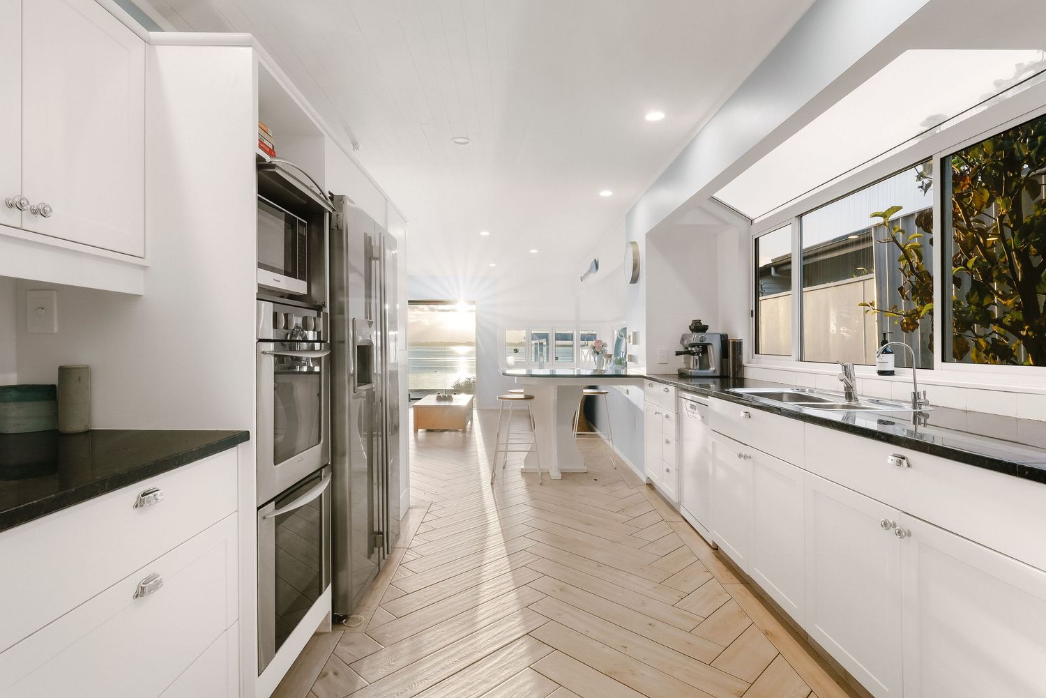 Contemporary white kitchen with herringbone flooring and sleek cabinetry.