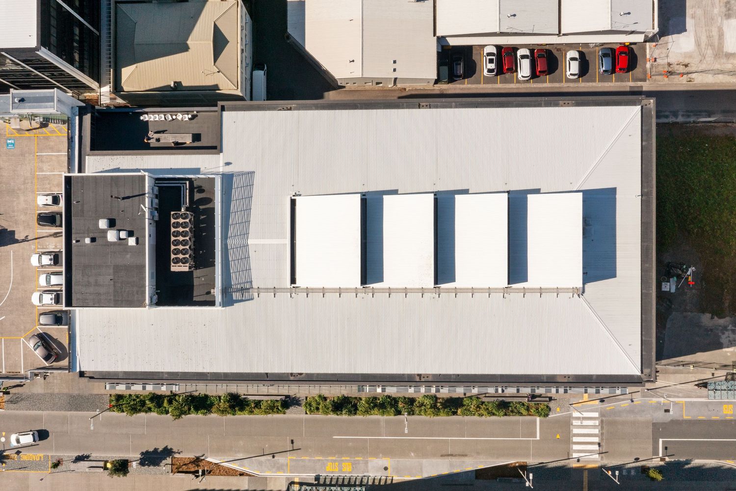 Overhead drone shot of modern commercial building complex with white rooftops and parking areas.