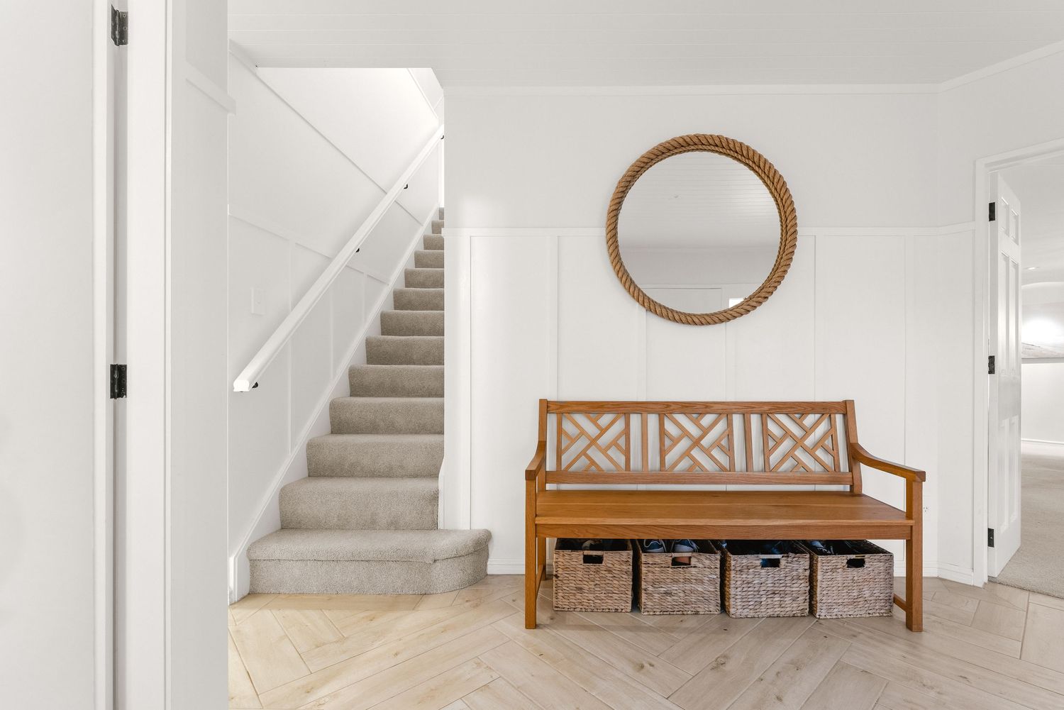Modern white entryway with wooden bench, round mirror, and carpeted stairs leading to second floor.