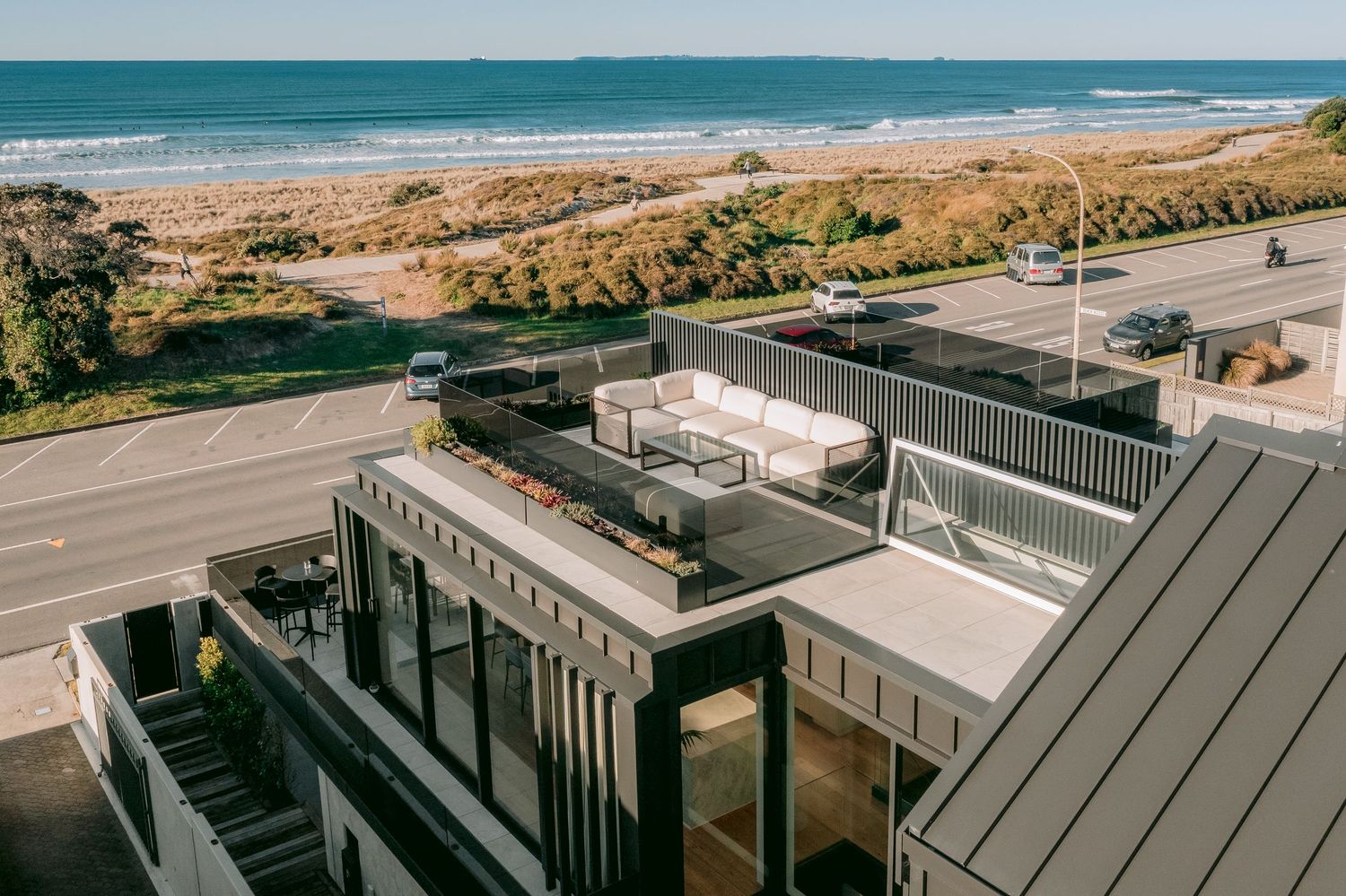 Luxury beachfront rooftop deck with modern furniture and coastal views along a scenic highway.