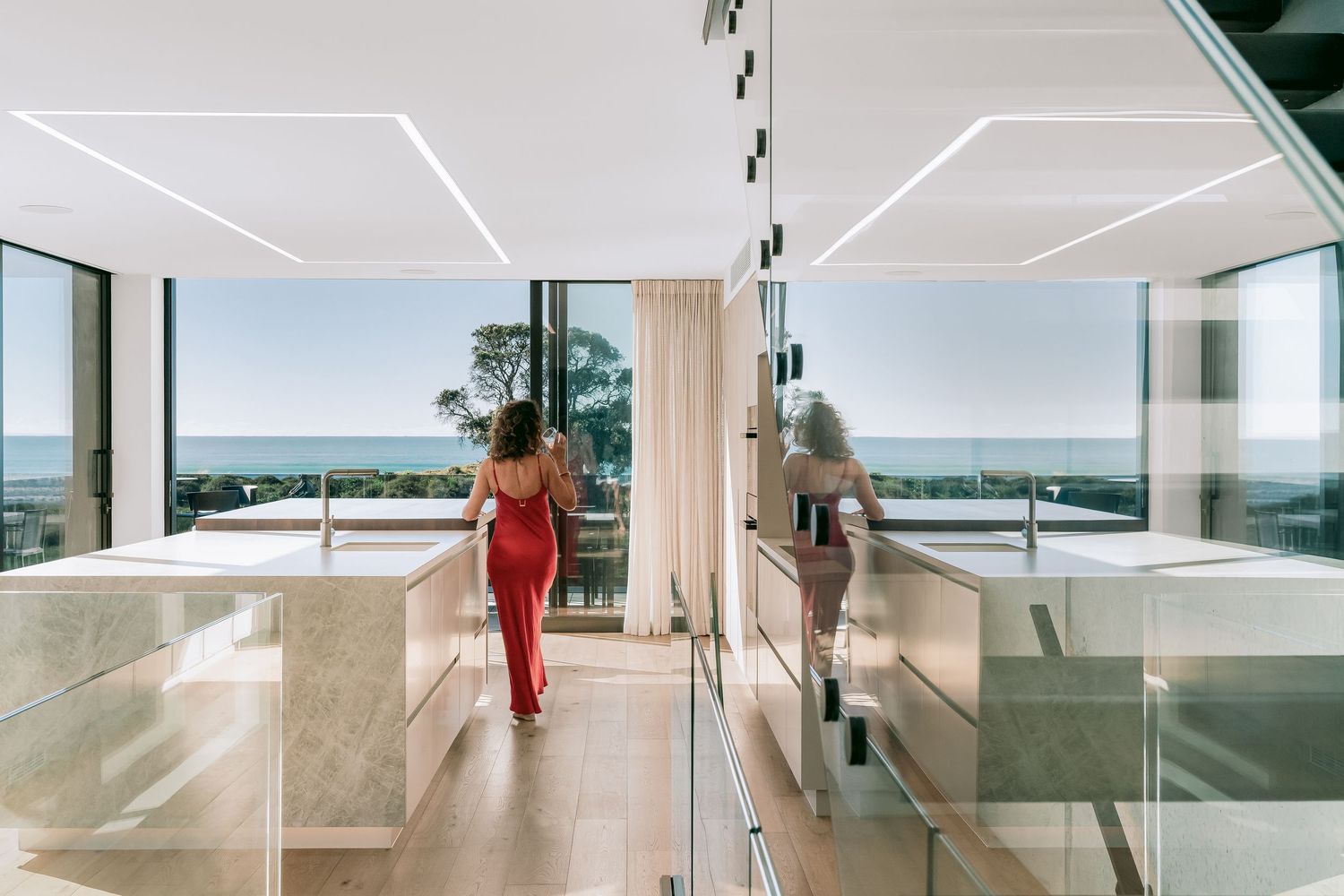 Modern luxury beach house interior with ocean views through floor-to-ceiling windows and sleek geometric lighting design.