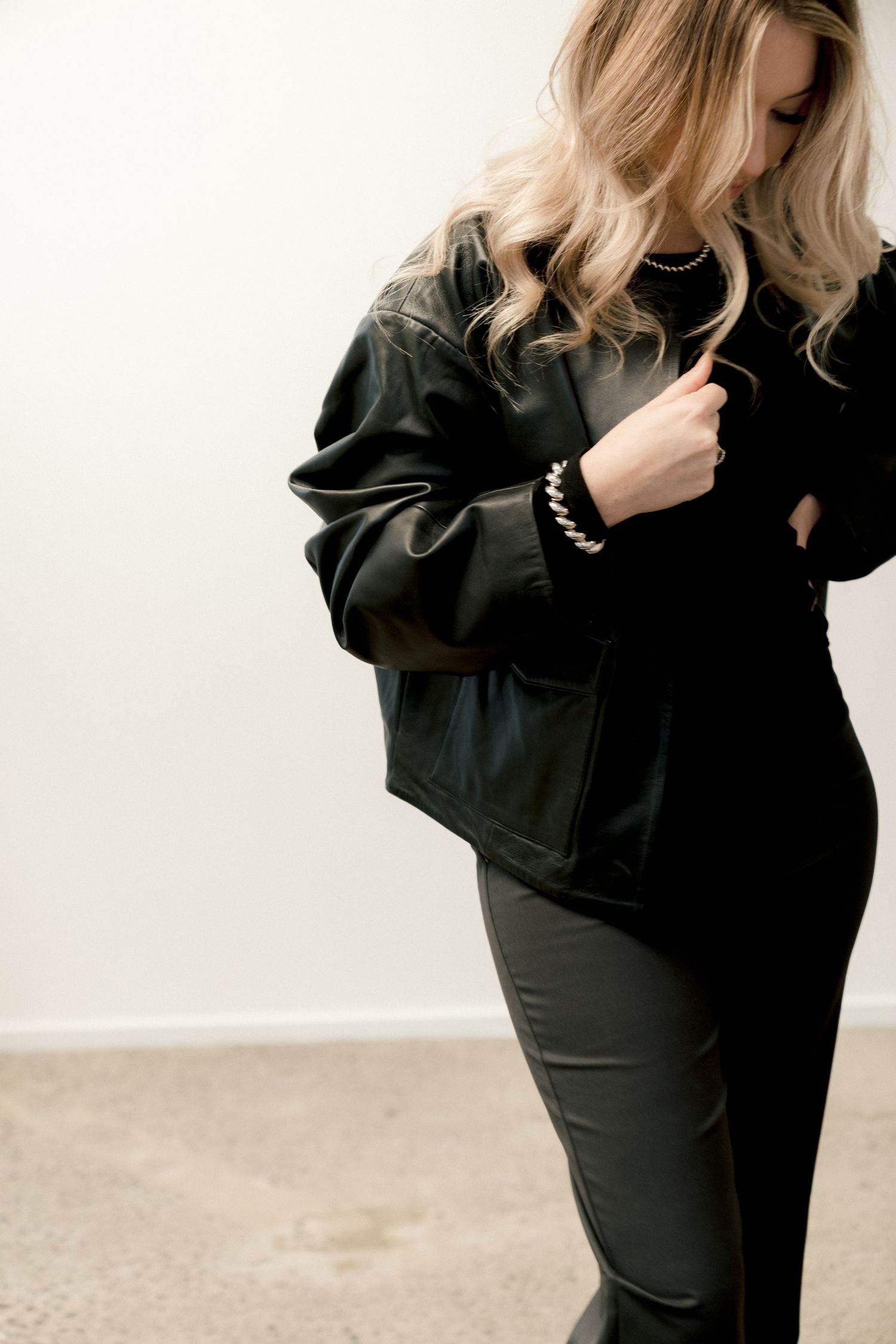 Woman wearing all black outfit with a cropped blazer and pants posing against white background.