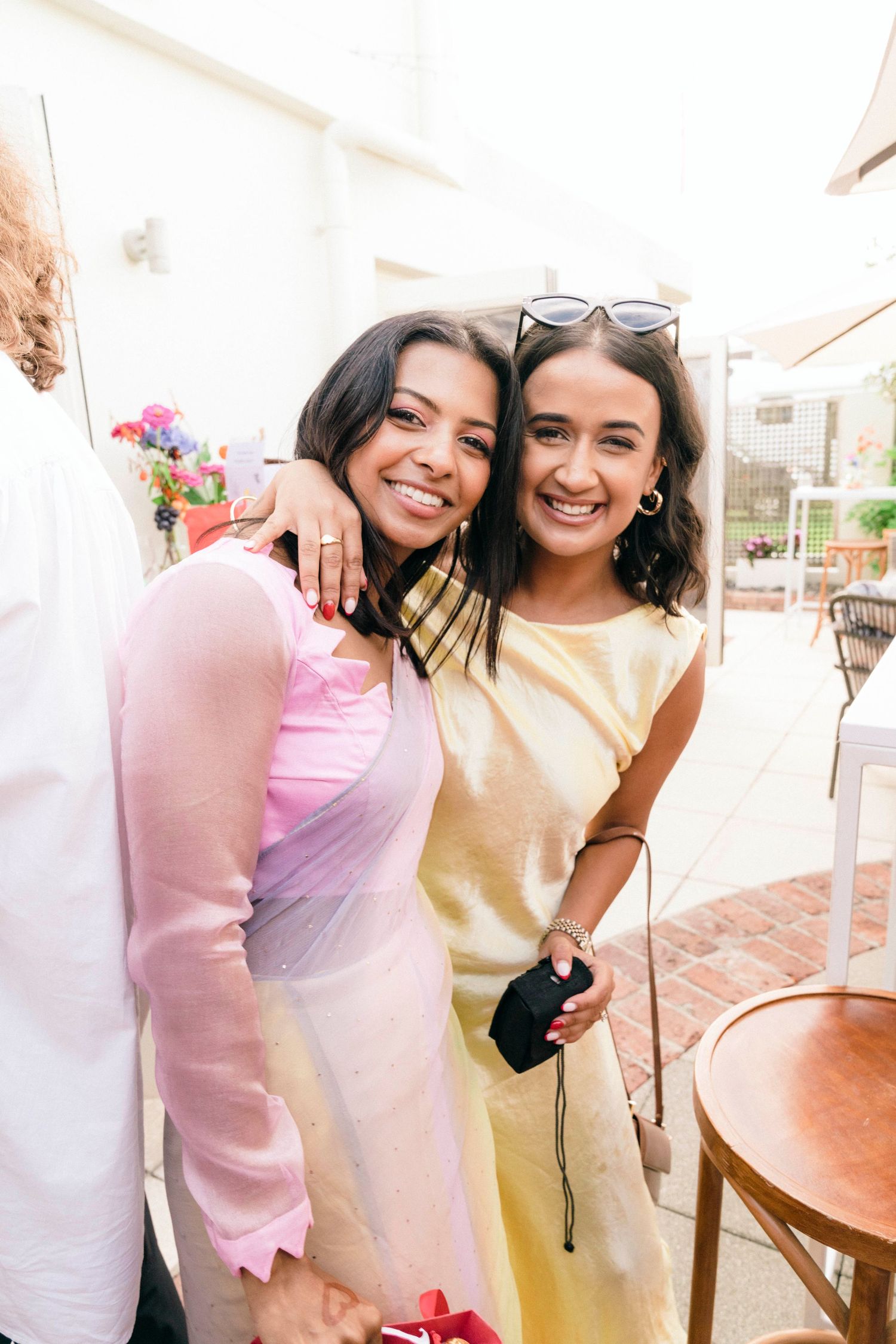 Two people in casual summer outfits smiling together in a bright outdoor setting.