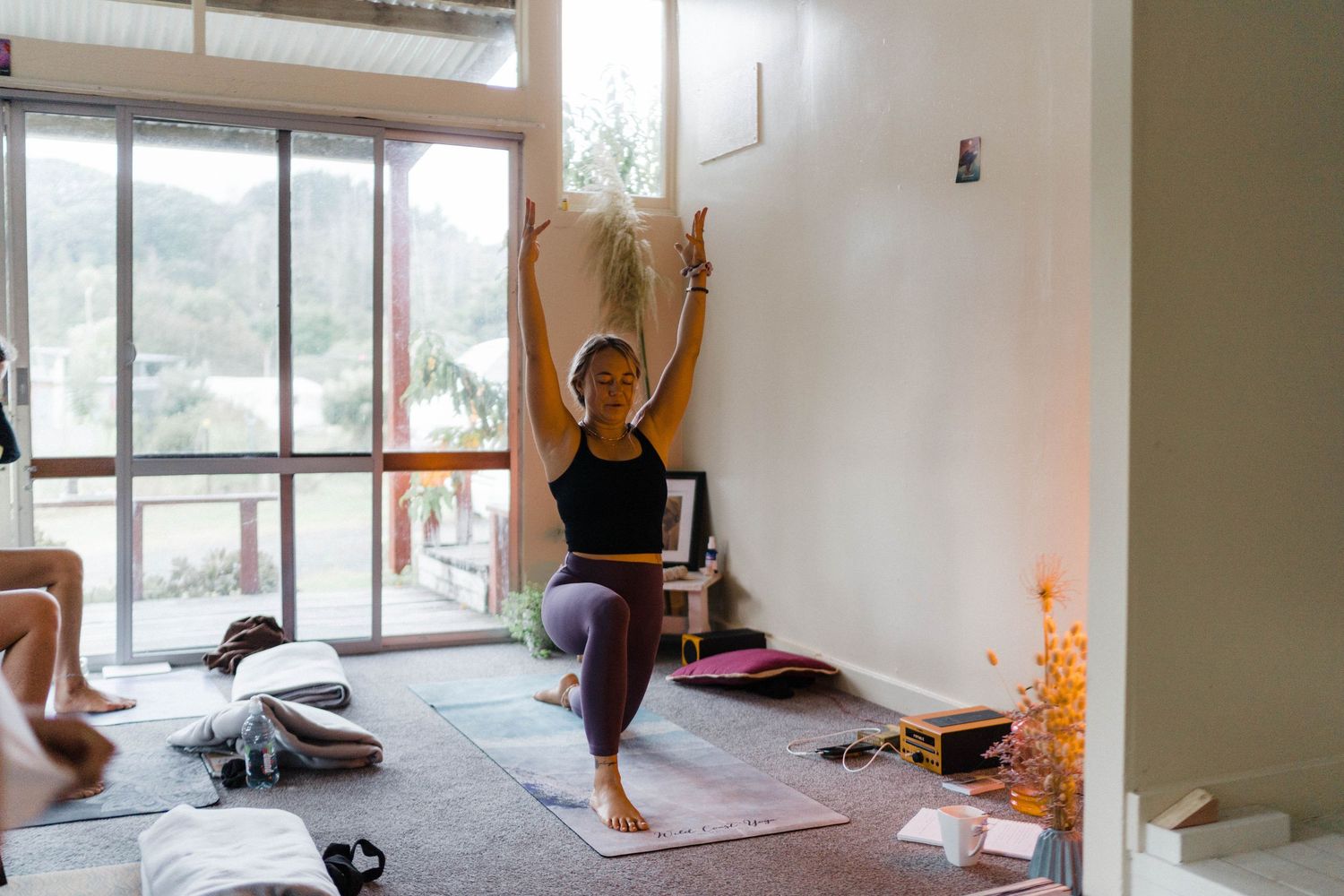 Someone doing a yoga pose in a bright indoor space with windows and yoga mats on the floor.