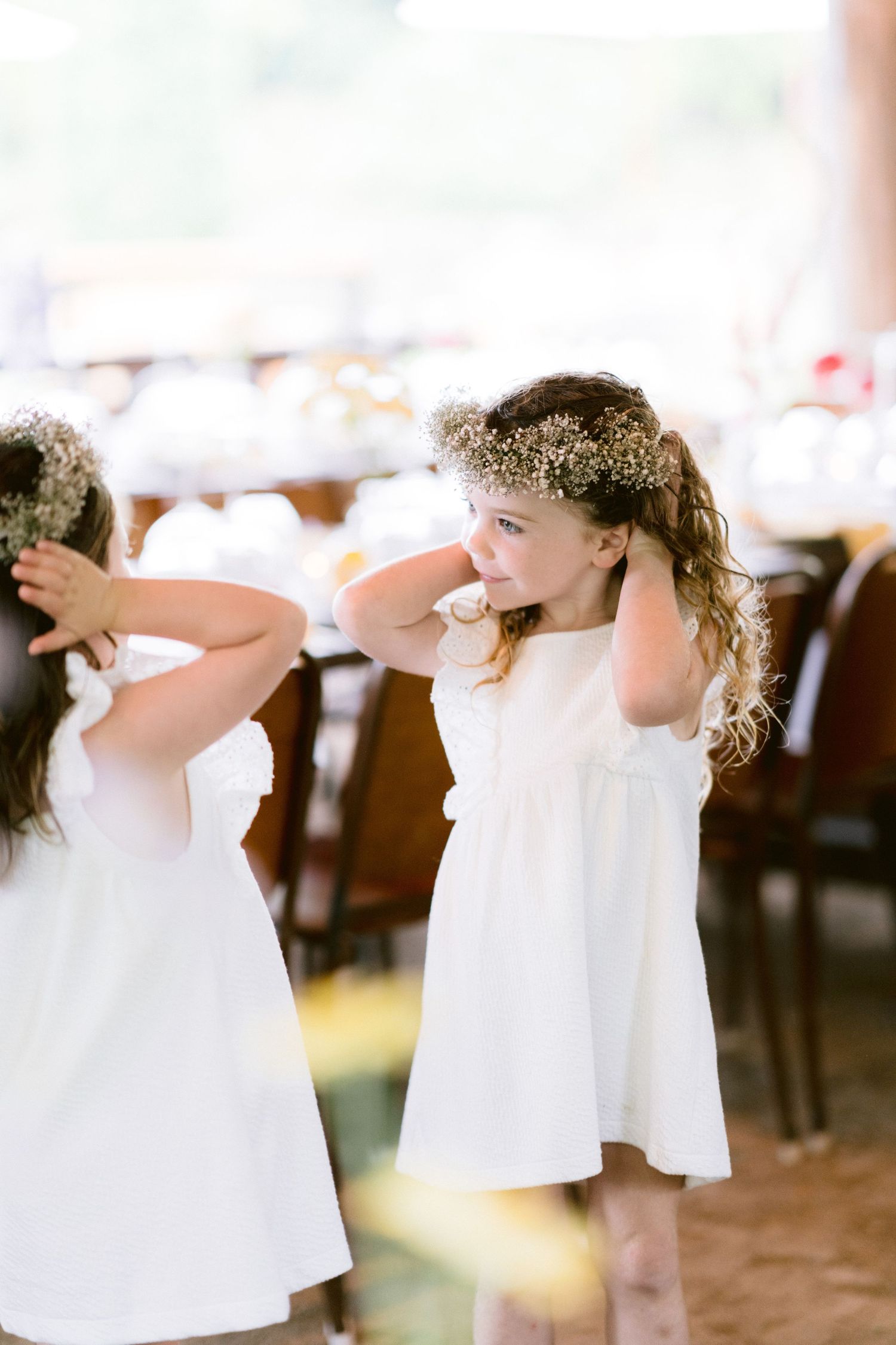 Two flower girls in white dresses wearing baby's breath crowns dance at a wedding reception.