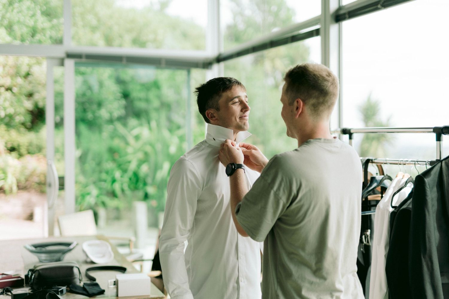 Two people in formal attire helping with wedding preparations indoors.