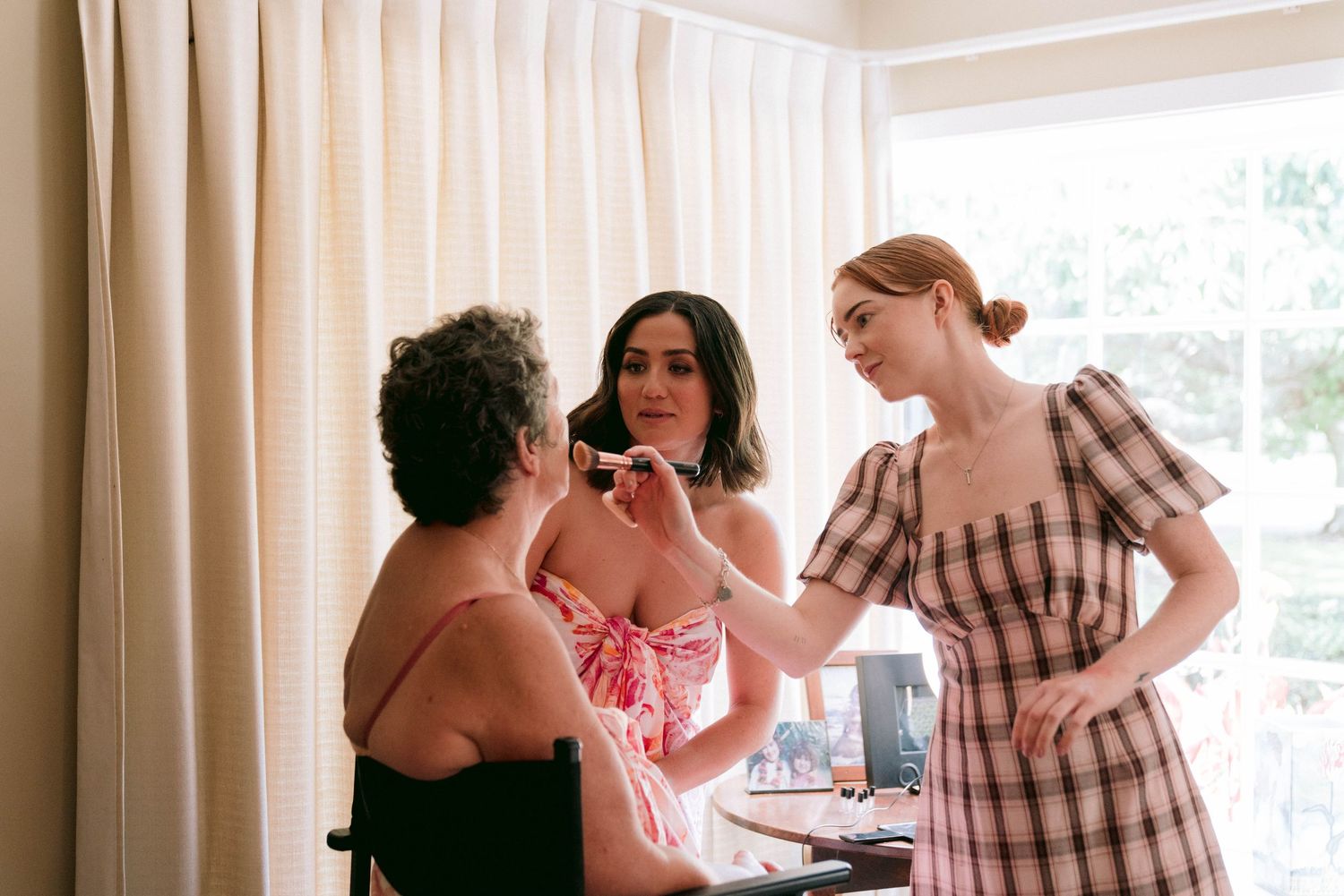 Wedding party getting ready in a bright room with white curtains.