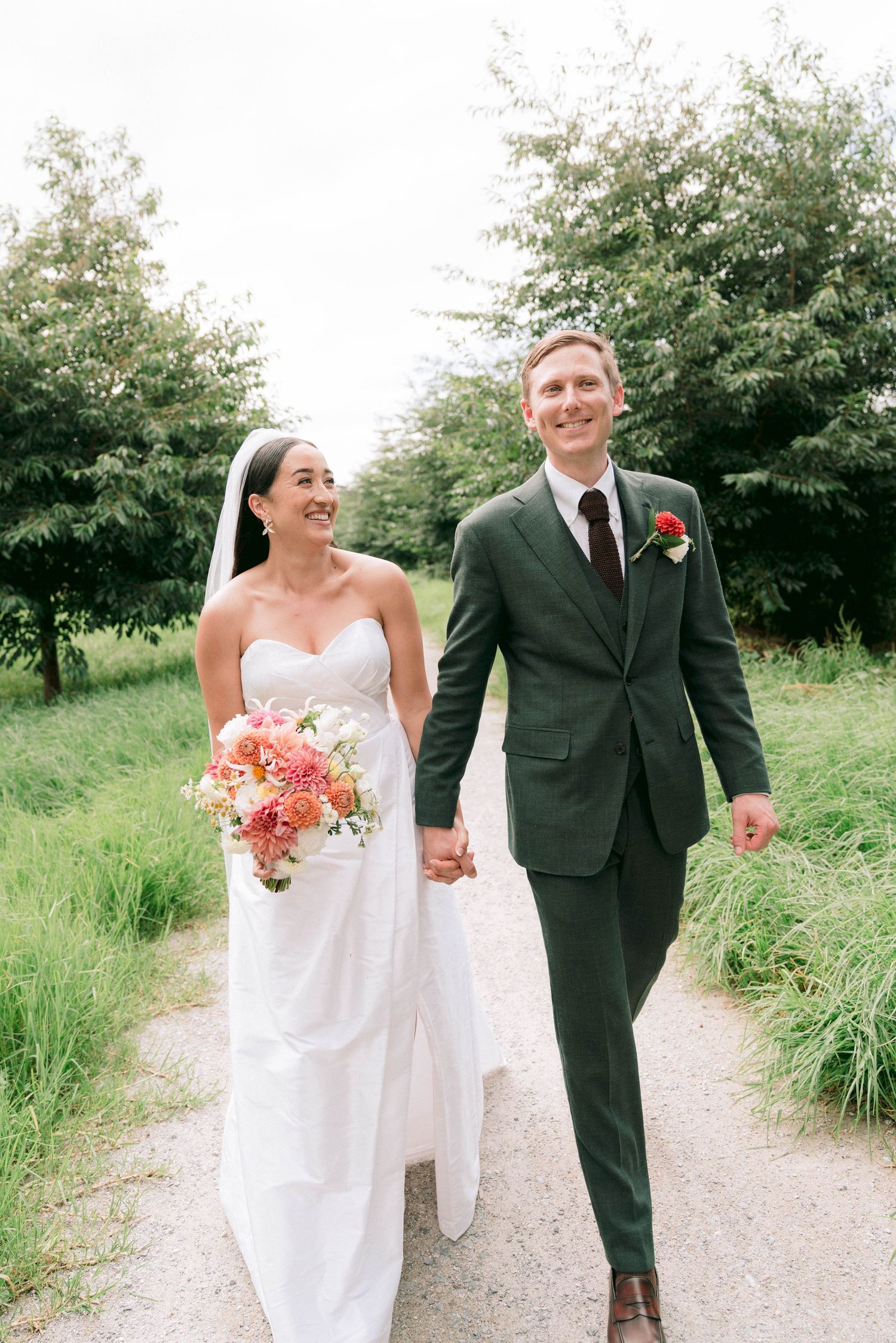 Couple walking hand in hand on a gravel path surrounded by greenery.