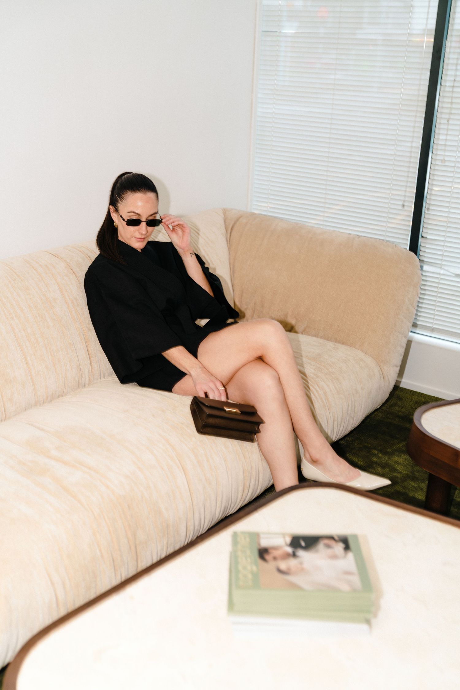 A sequence of someone lounging in a beige couch reading a book while wearing black clothing and sunglasses.