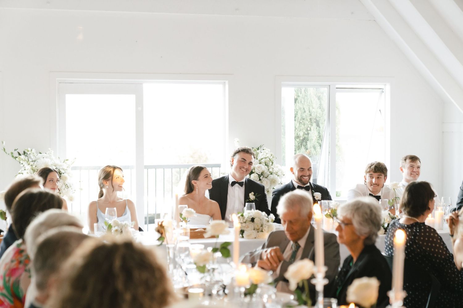 Wedding guests gather in bright, airy venue with white vaulted ceilings for celebration.