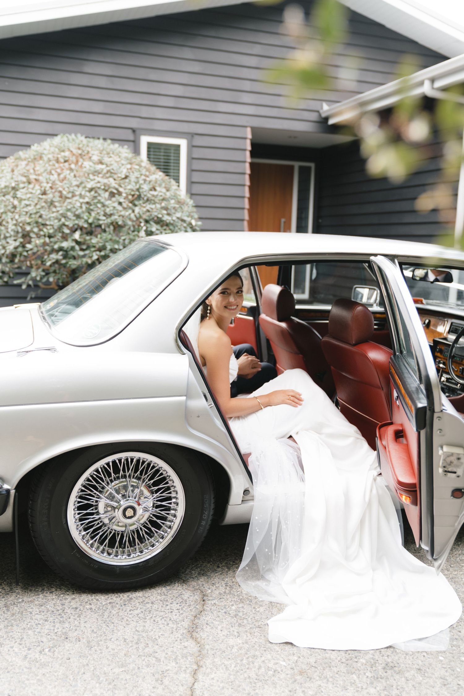 Classic white vintage car with silver spoke wheels parked outside on gravel.