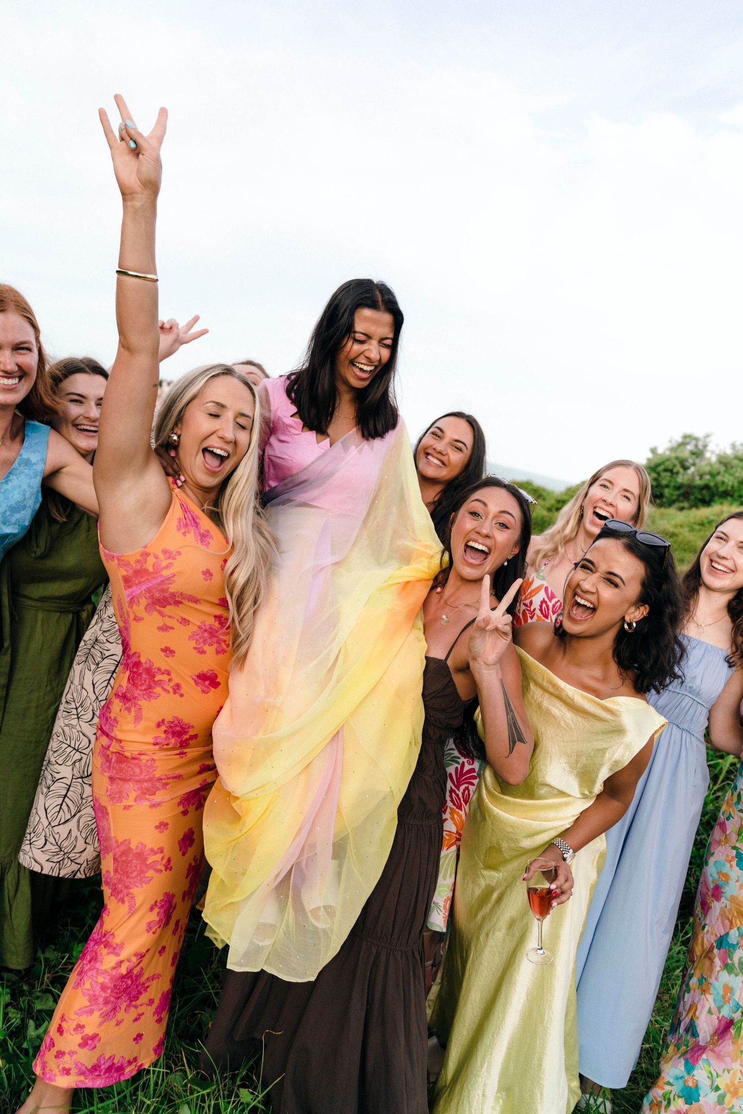 Group of friends in vibrant dresses celebrating outdoors with energetic poses and laughter.
