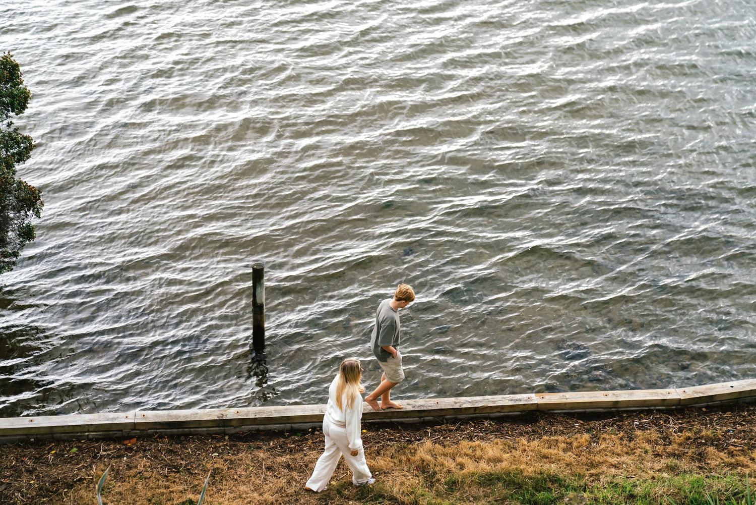 Figure walking along waterfront path beside rippling water surface.