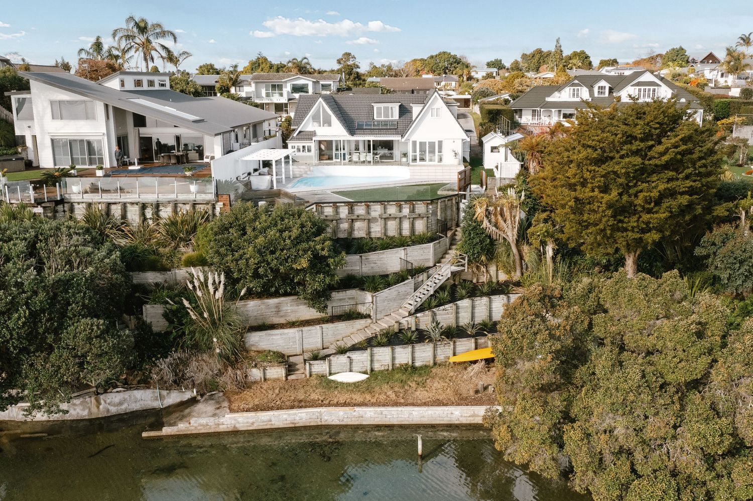 Aerial view of white coastal homes with terraced landscaping leading down to waterfront.