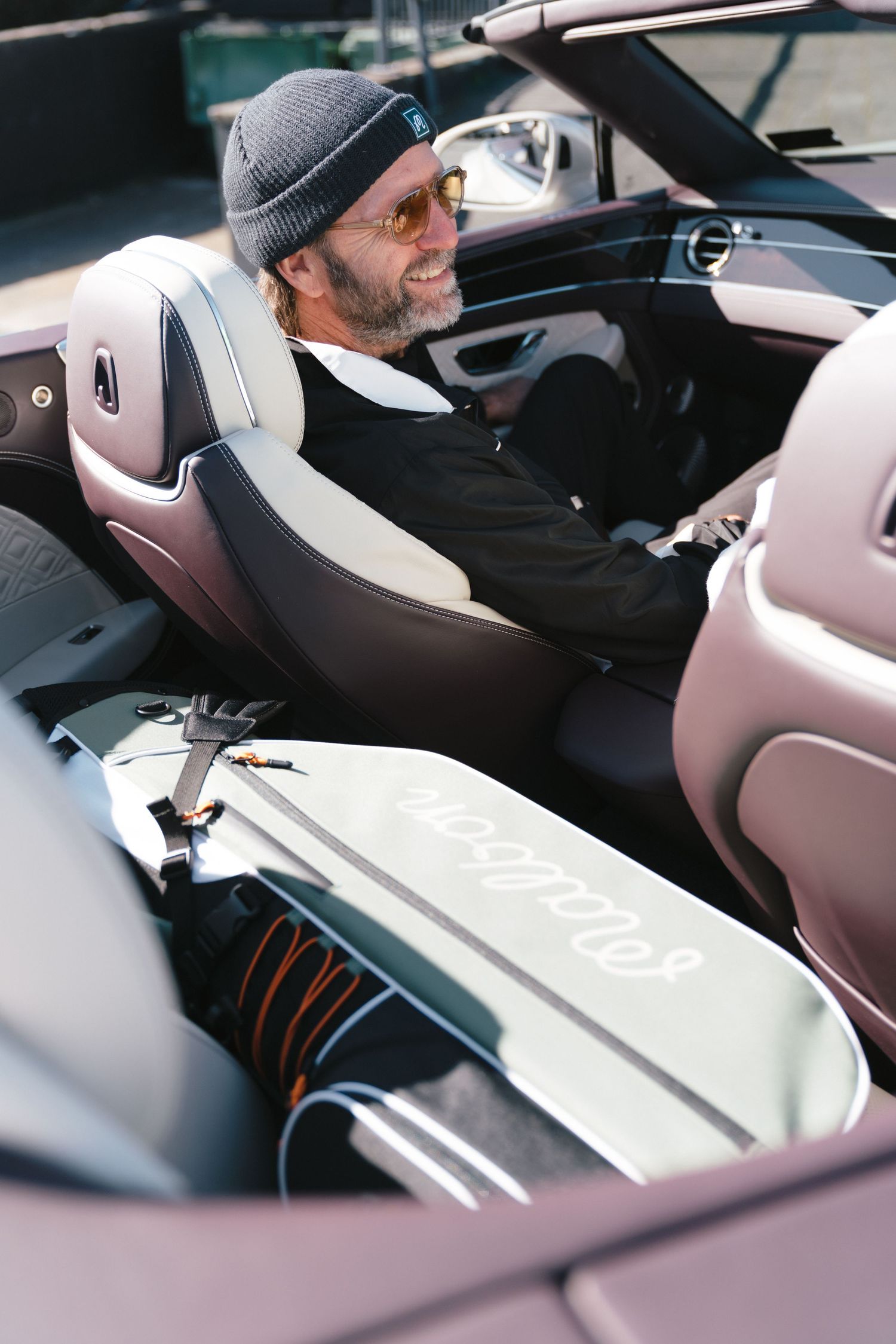 Driver in beanie and sunglasses sits in luxury convertible with custom interior and contrasting leather seats.