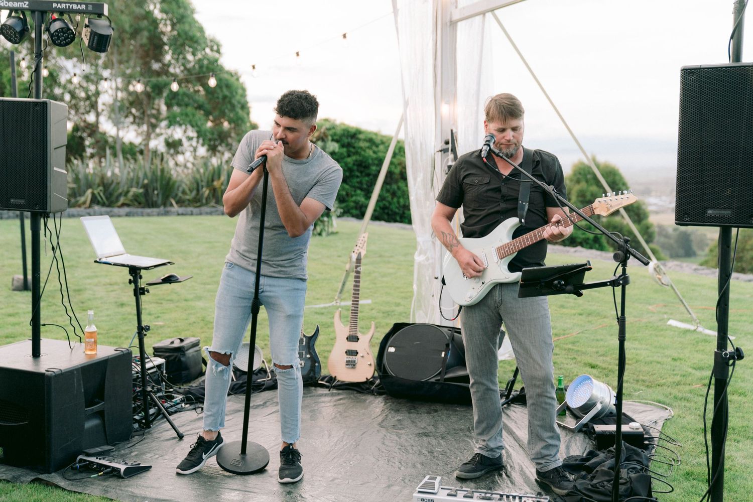 Live band performs at outdoor wedding with singer and guitarist on stage with professional equipment.