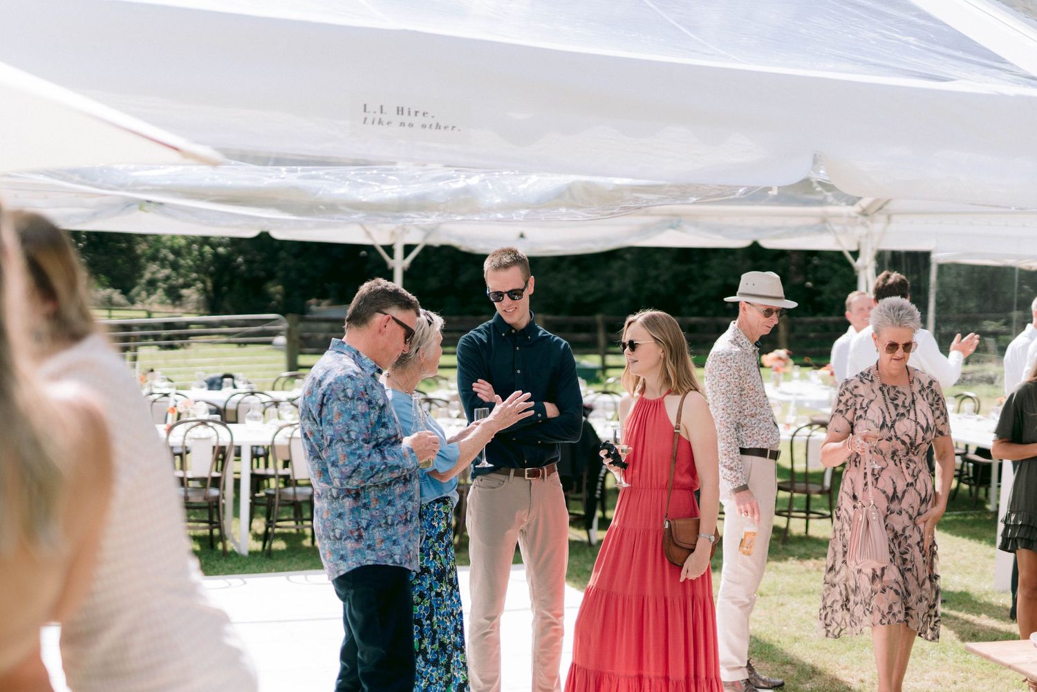 Guests mingling under white tent canopy at outdoor event.