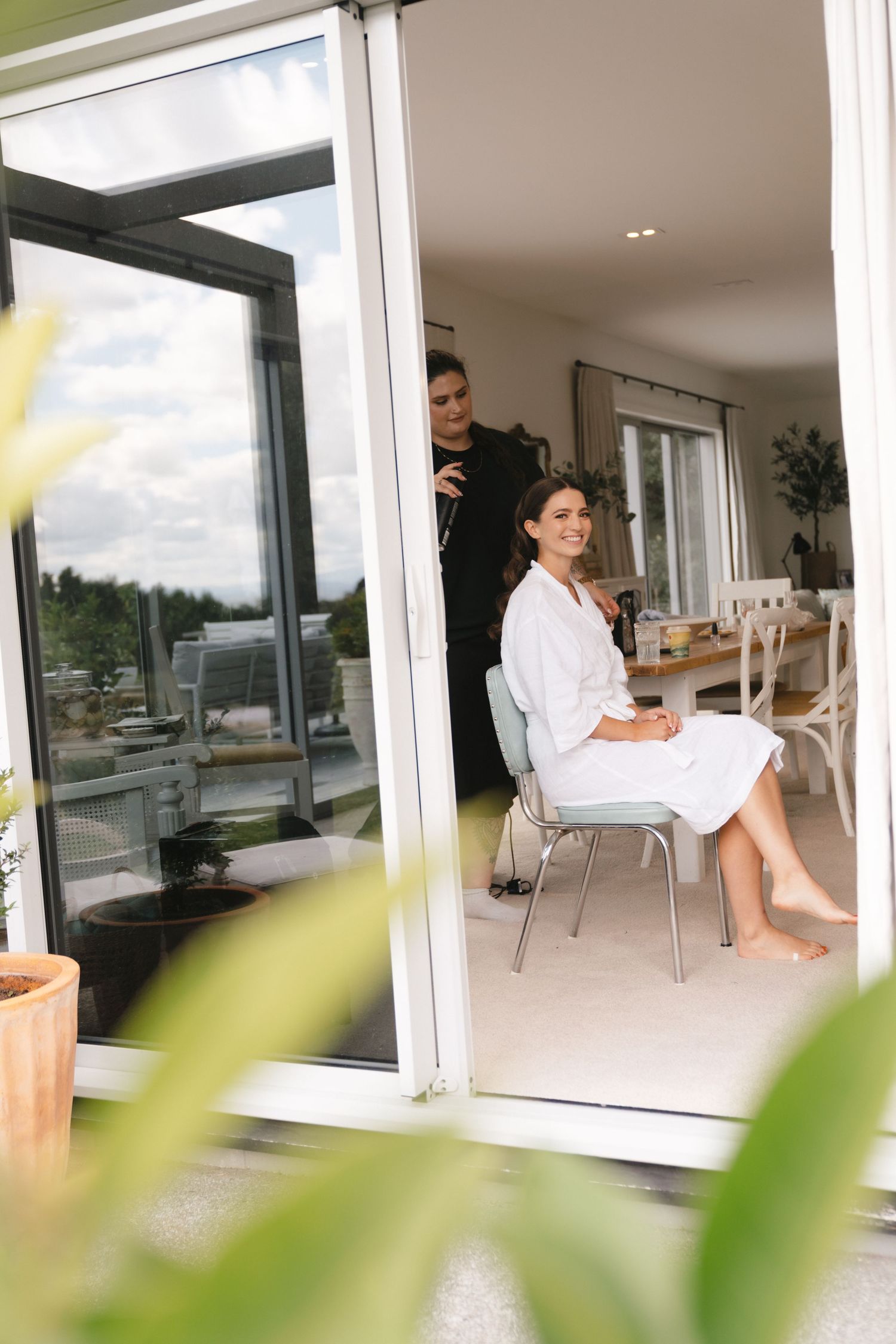Two people relax in a bright modern room with large windows overlooking greenery and scenic views.