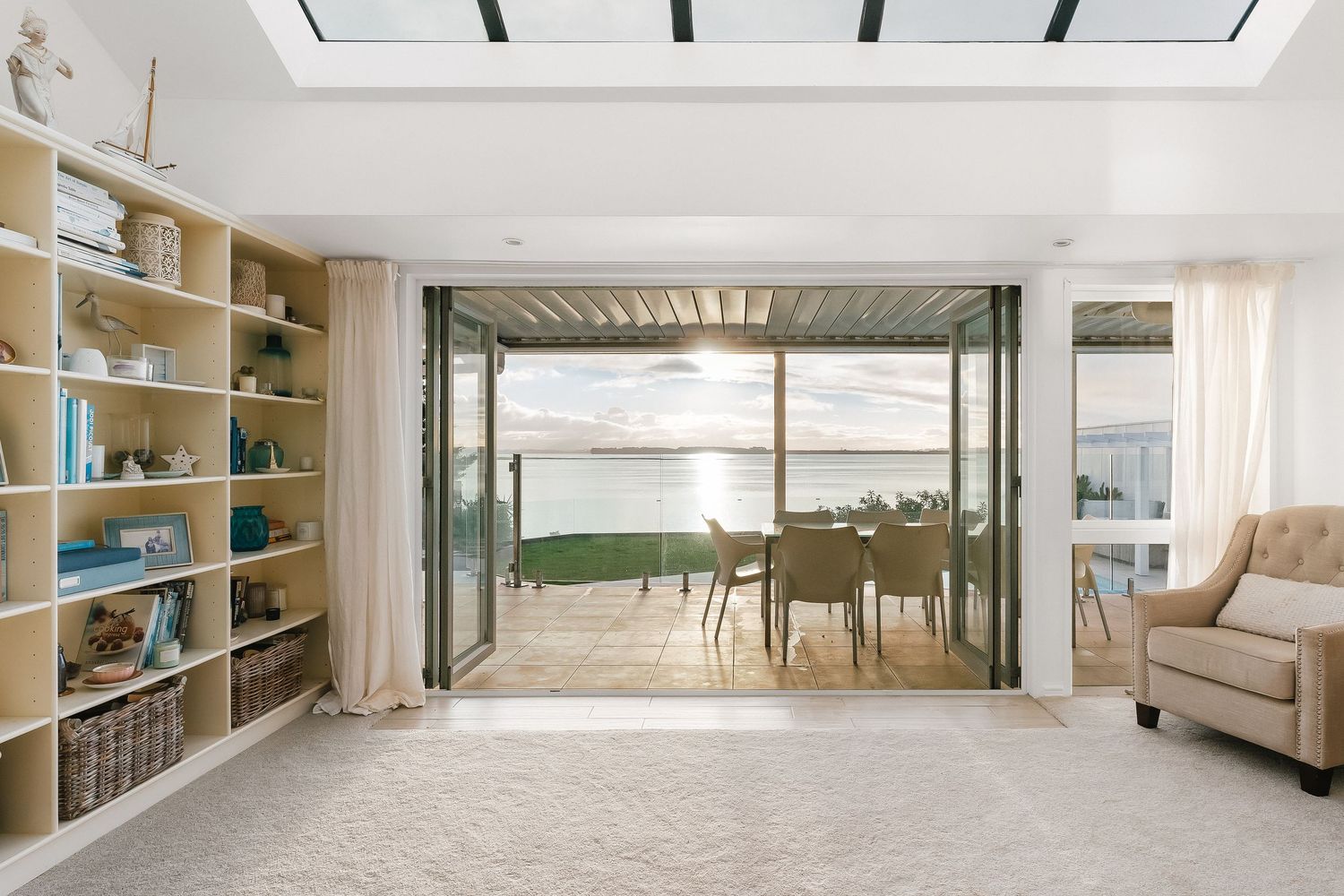Contemporary living room with built-in bookshelves and folding glass doors opening to waterfront views.