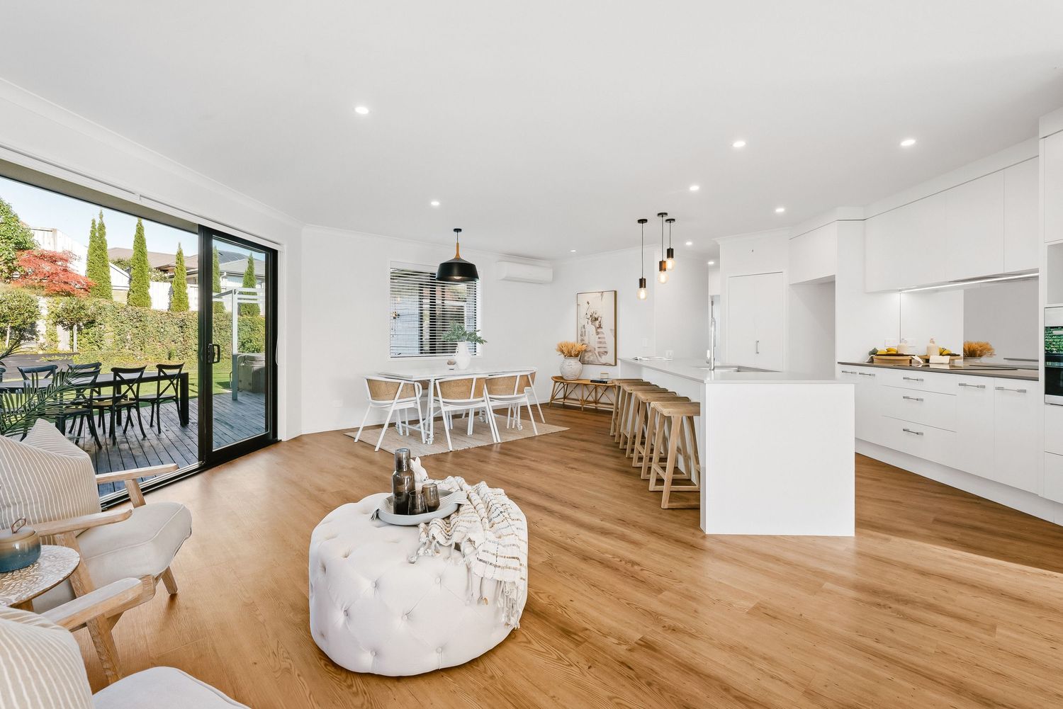 Modern open concept living area with white kitchen, hardwood floors and contemporary furnishings overlooking outdoor space.