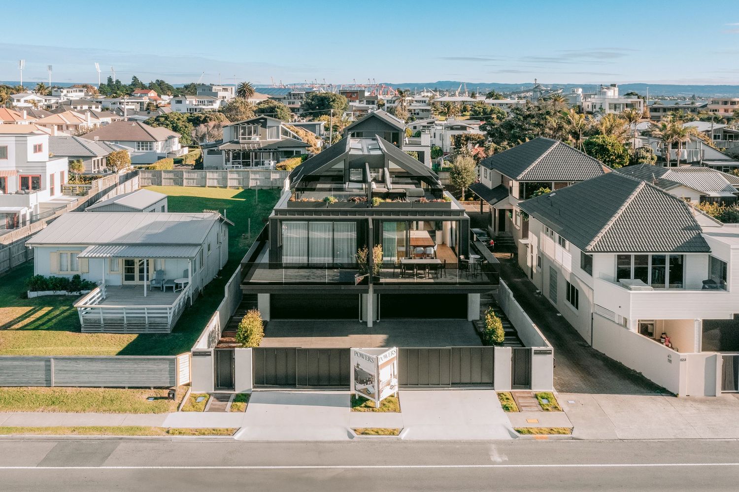 A panoramic street view shows modern residential buildings with garages along a quiet suburban neighborhood in sunlight.
