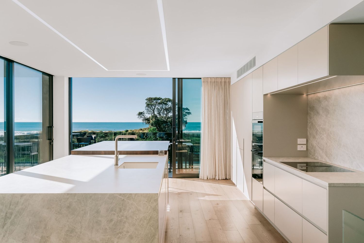 Modern oceanfront apartment interior with hardwood floors, white kitchen, and large sliding doors opening to a balcony with sea views.