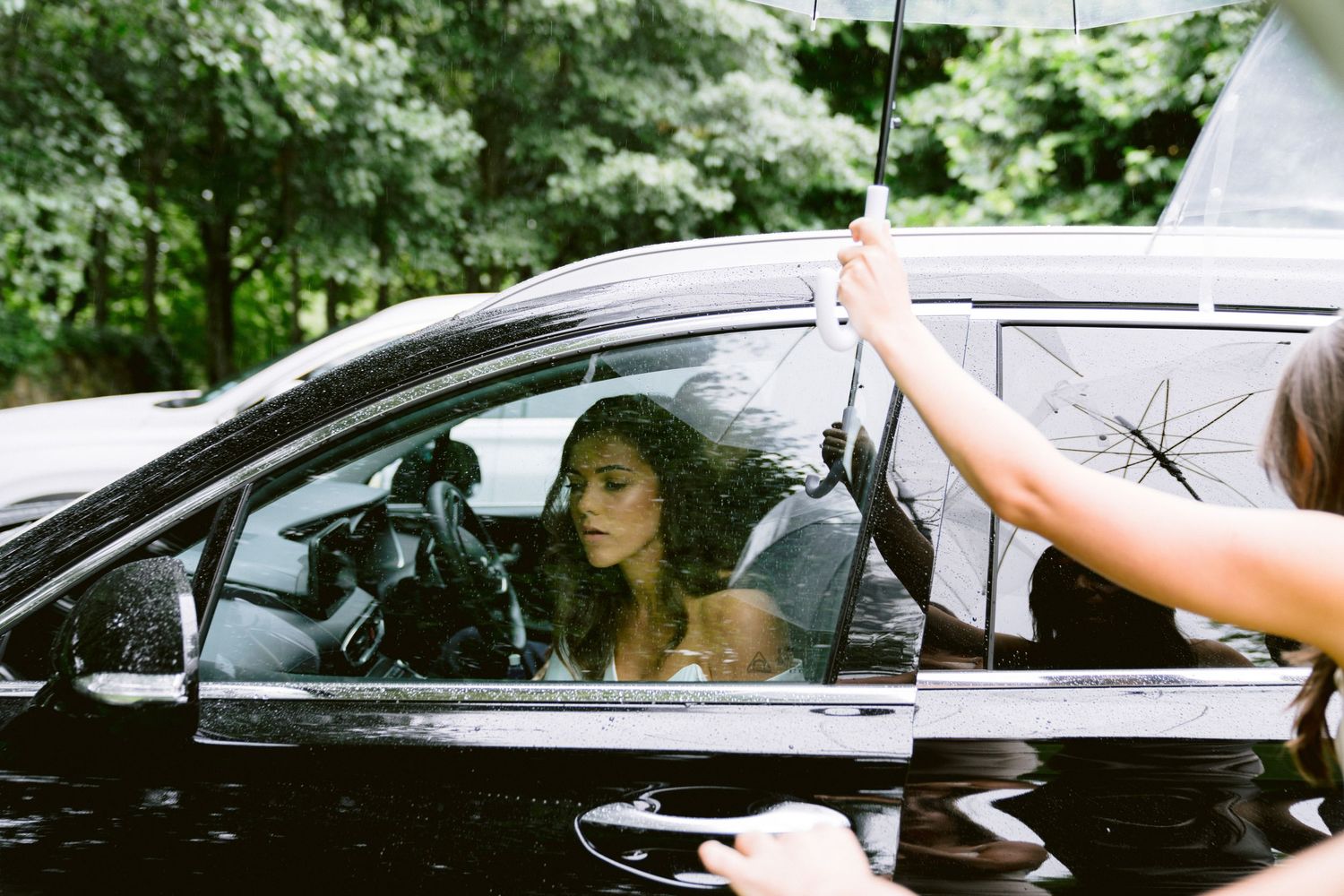 A black car on a winding road through lush green trees while someone waves from outside.