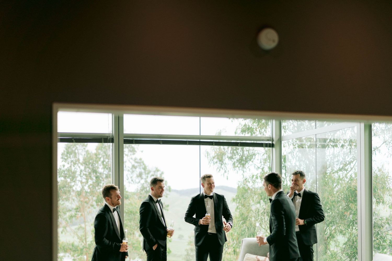 Wedding party gathered by large windows in formal attire.