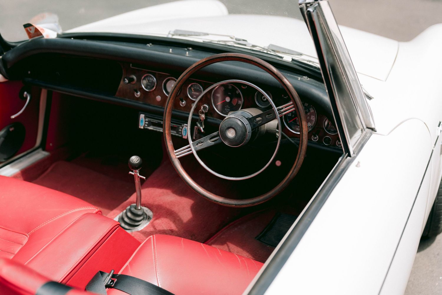 Classic vintage car interior featuring red leather seats and wooden steering wheel.