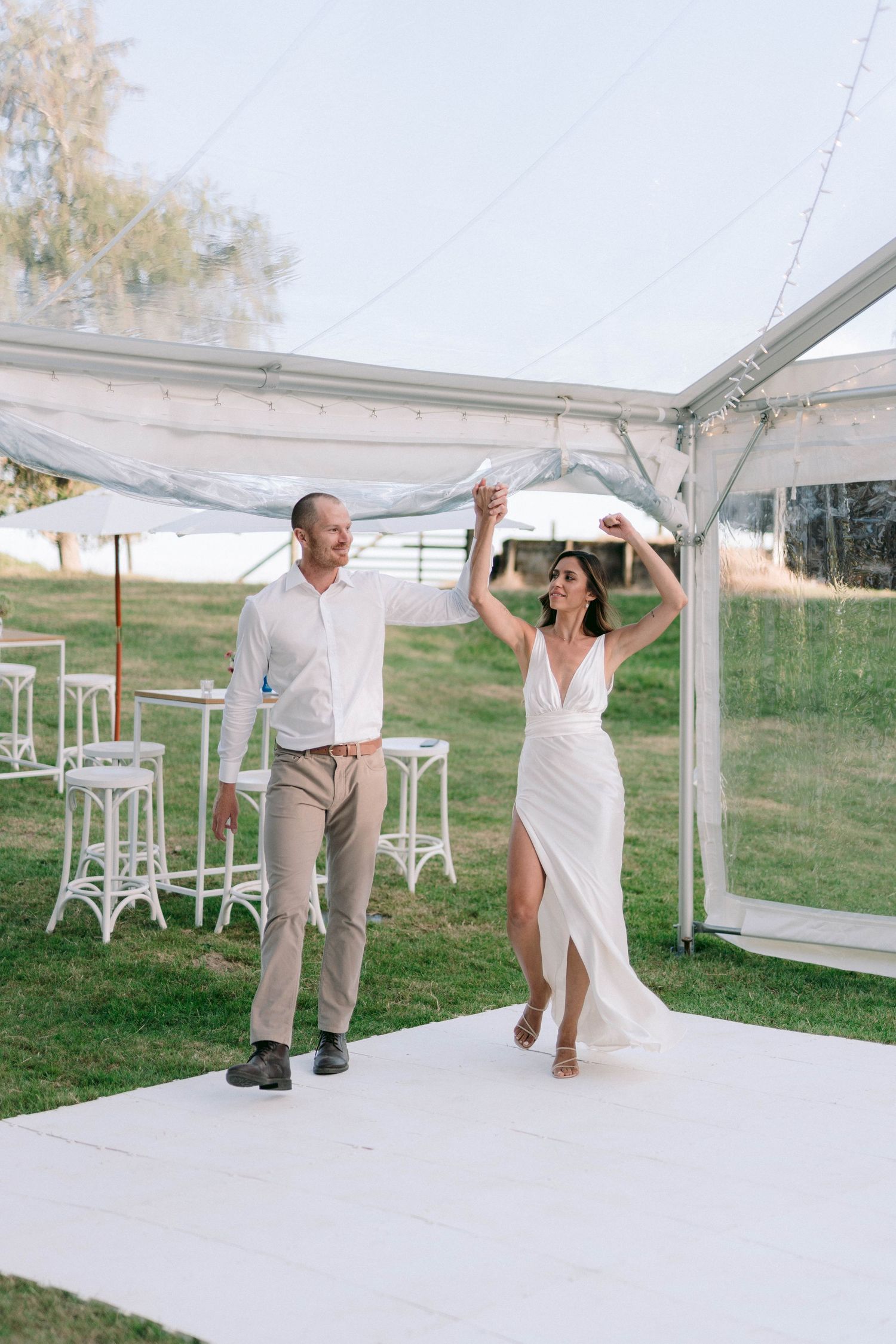 A couple dances together under a white outdoor tent during a wedding celebration.