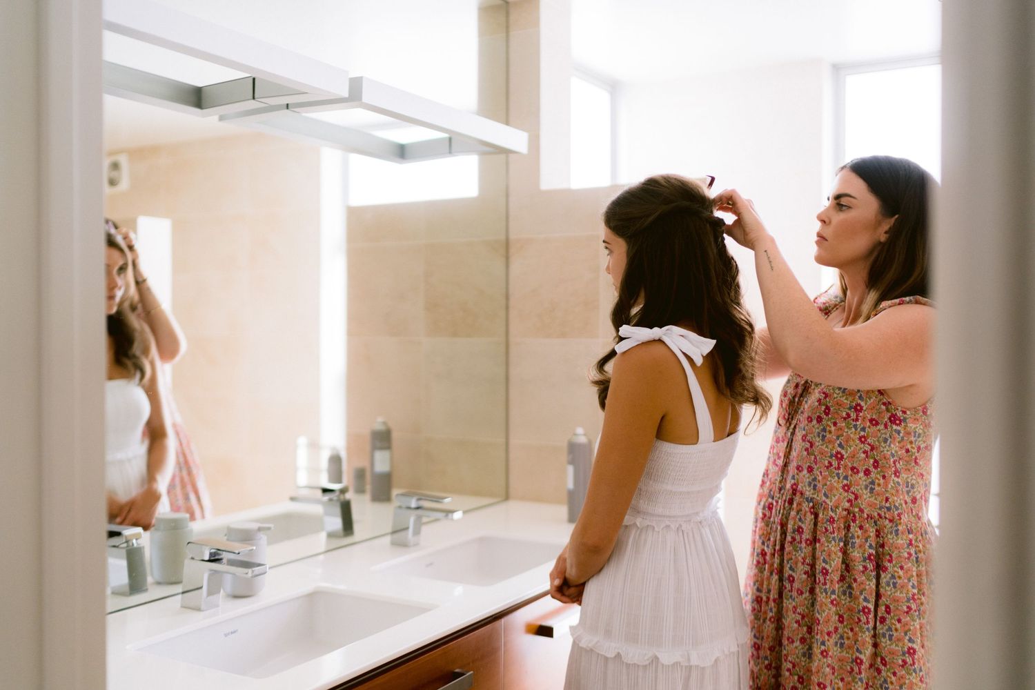 Two people getting ready in a modern bathroom with white countertops and bright lighting.