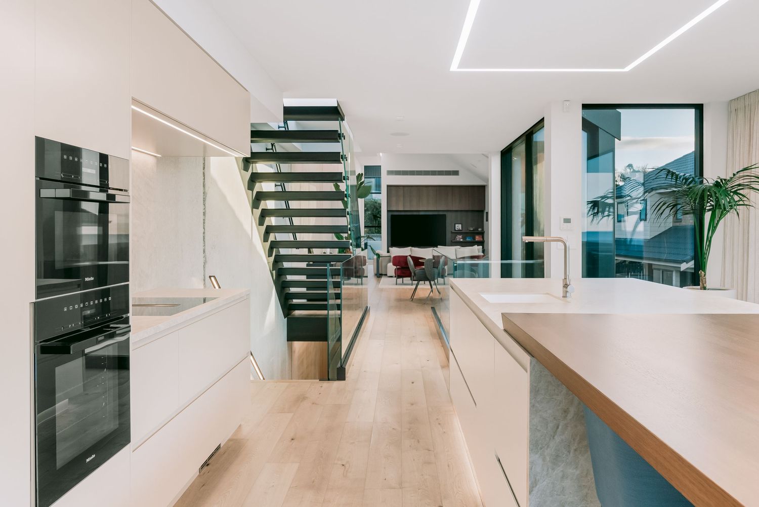 Contemporary open concept kitchen with floating staircase, light wood floors and sleek black appliances.