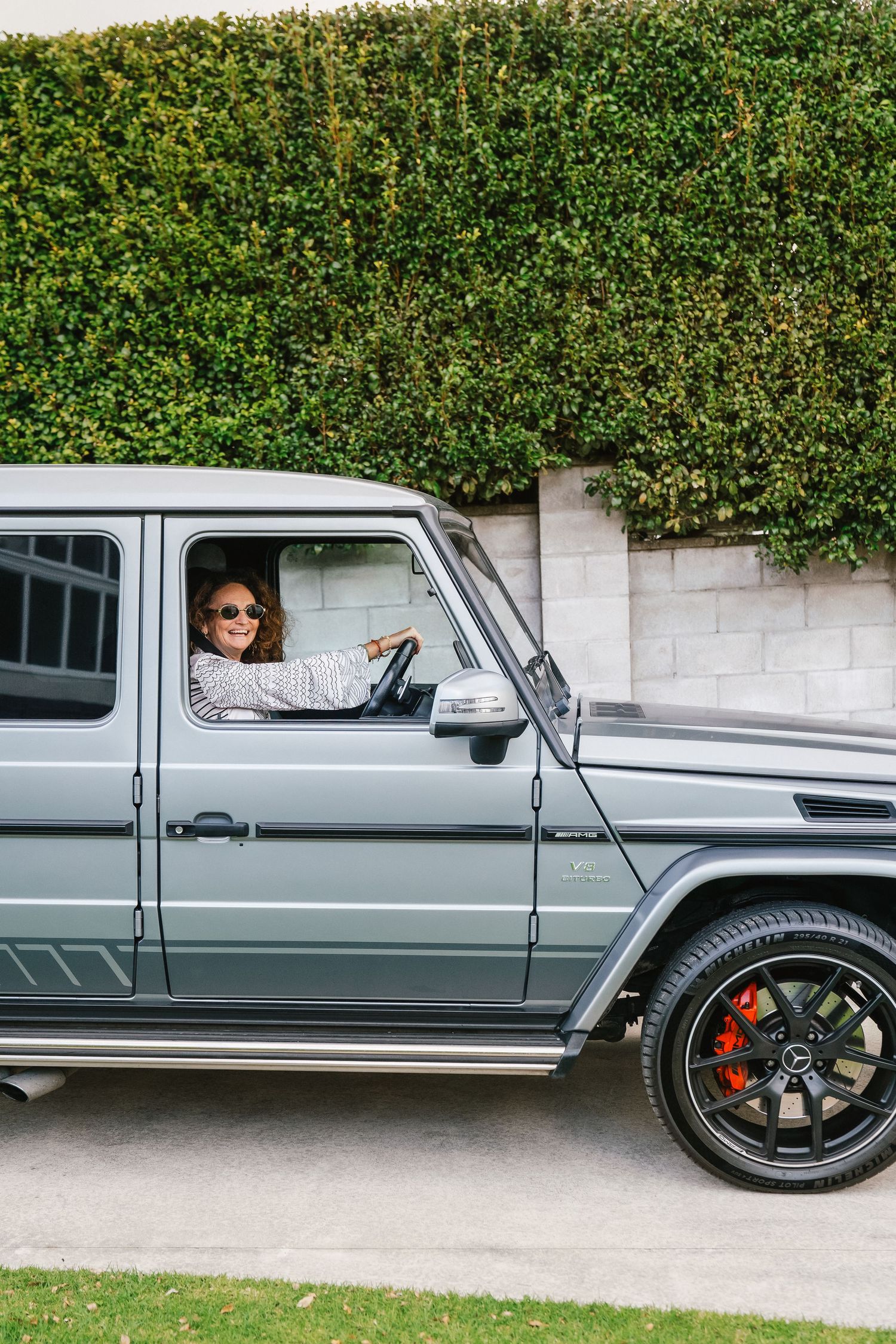 Silver Mercedes G-Wagon parked in front of a lush green hedge wall.