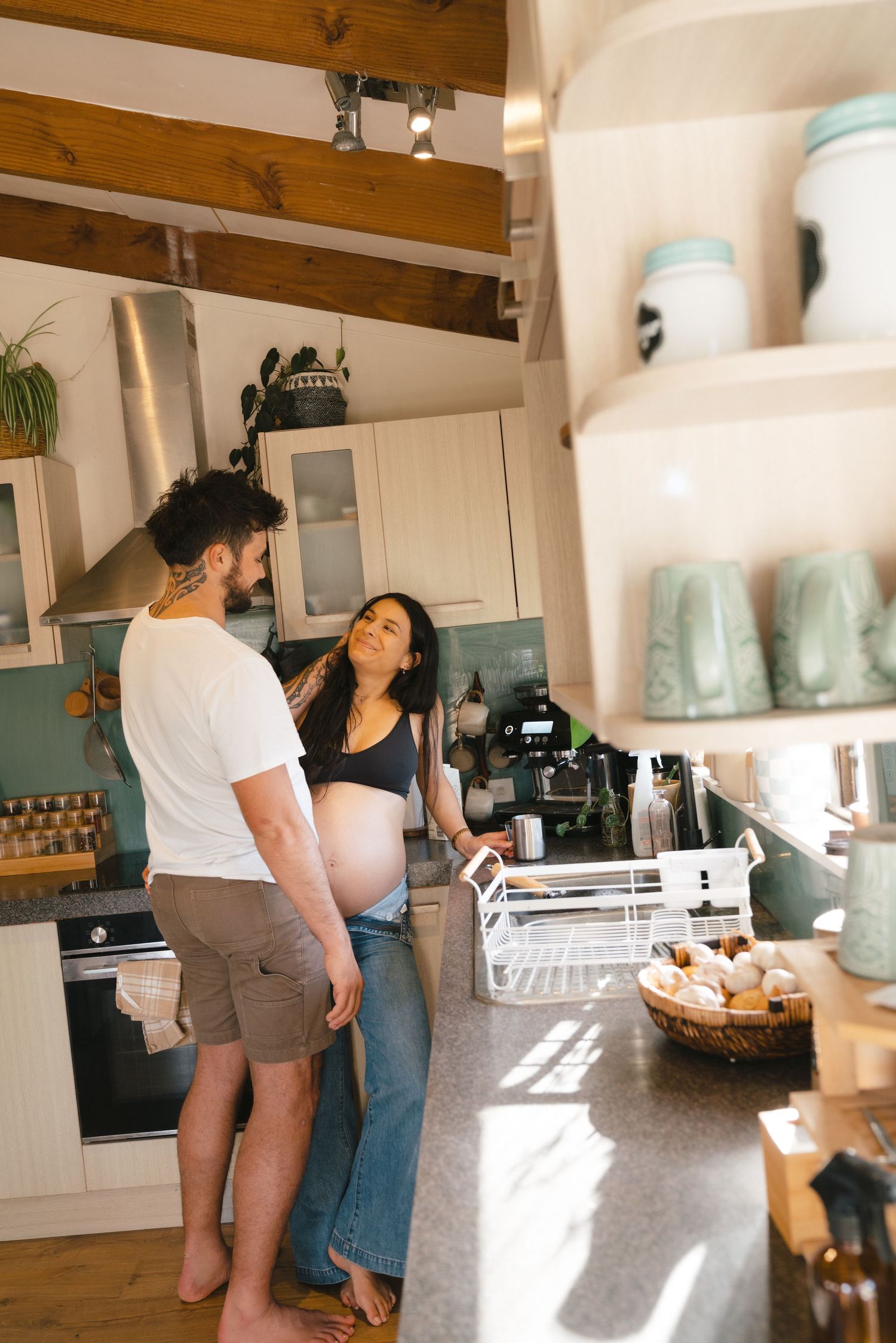 Sun-filled modern kitchen scene with a couple sharing a casual moment among rustic wooden beams and jars.